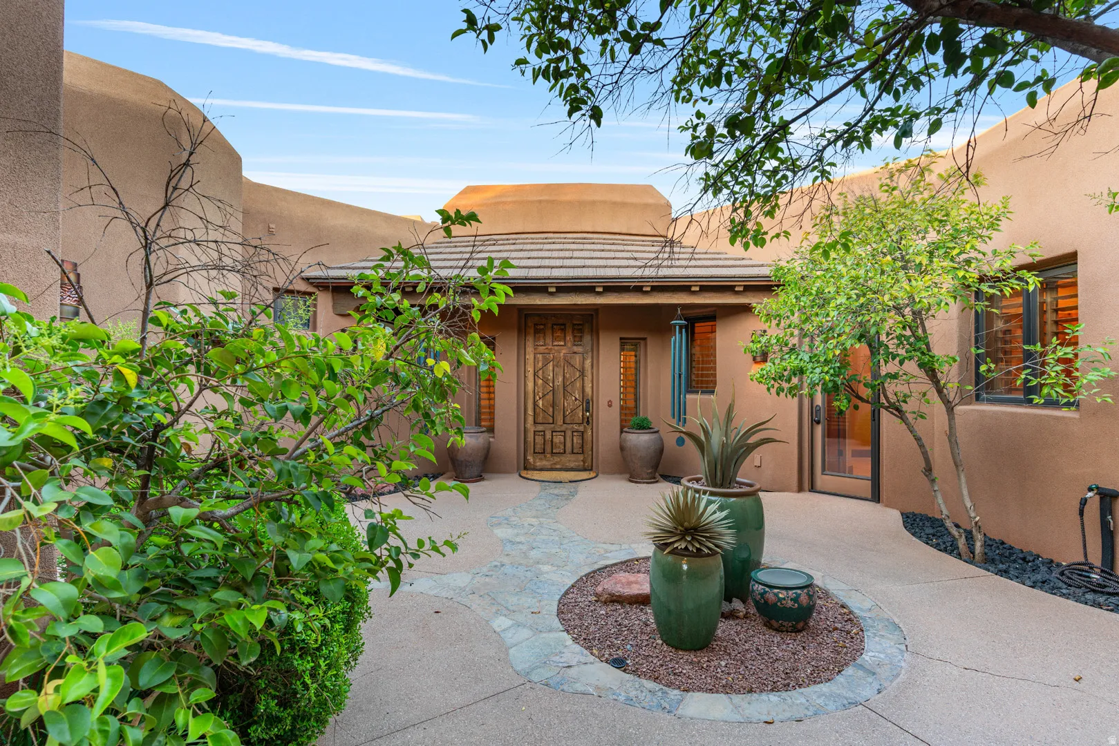 Entry courtyard featuring a carved wood front door, flagstone path, stucco exterior, and mature landscaping