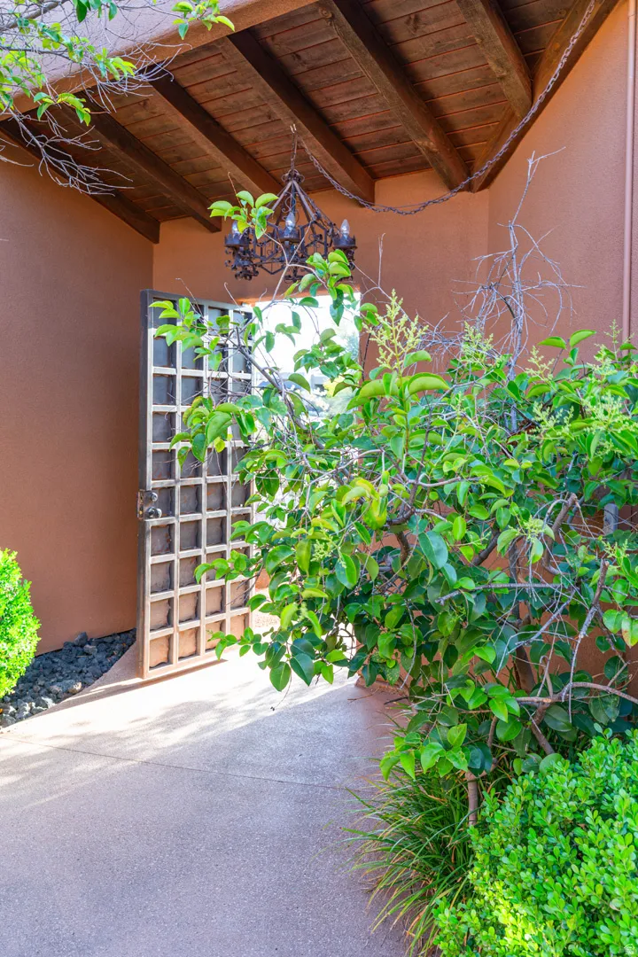 Covered entry with exposed wood beam ceiling, wrought iron chandelier, and a decorative gate
