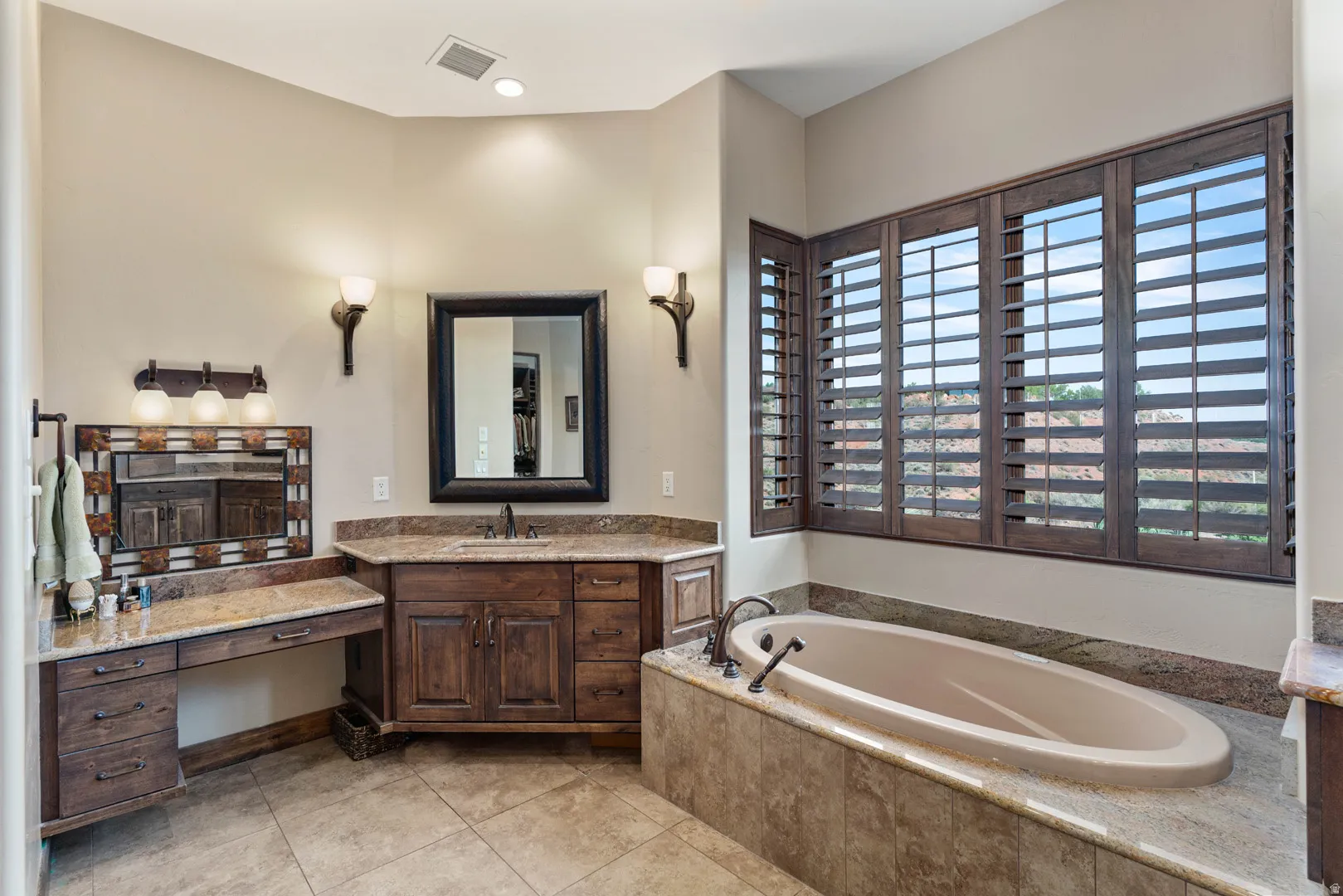 Bathroom featuring a built-in soaking tub, wood plantation shutters, a vanity with a granite countertop, a built-in dressing table, and tile flooring