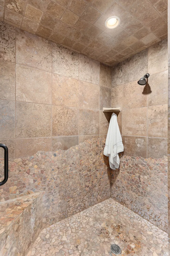Primary tiled shower enclosure featuring a corner bench, integrated shower niche, mosaic pebble-style flooring, and a ceiling-mounted light fixture