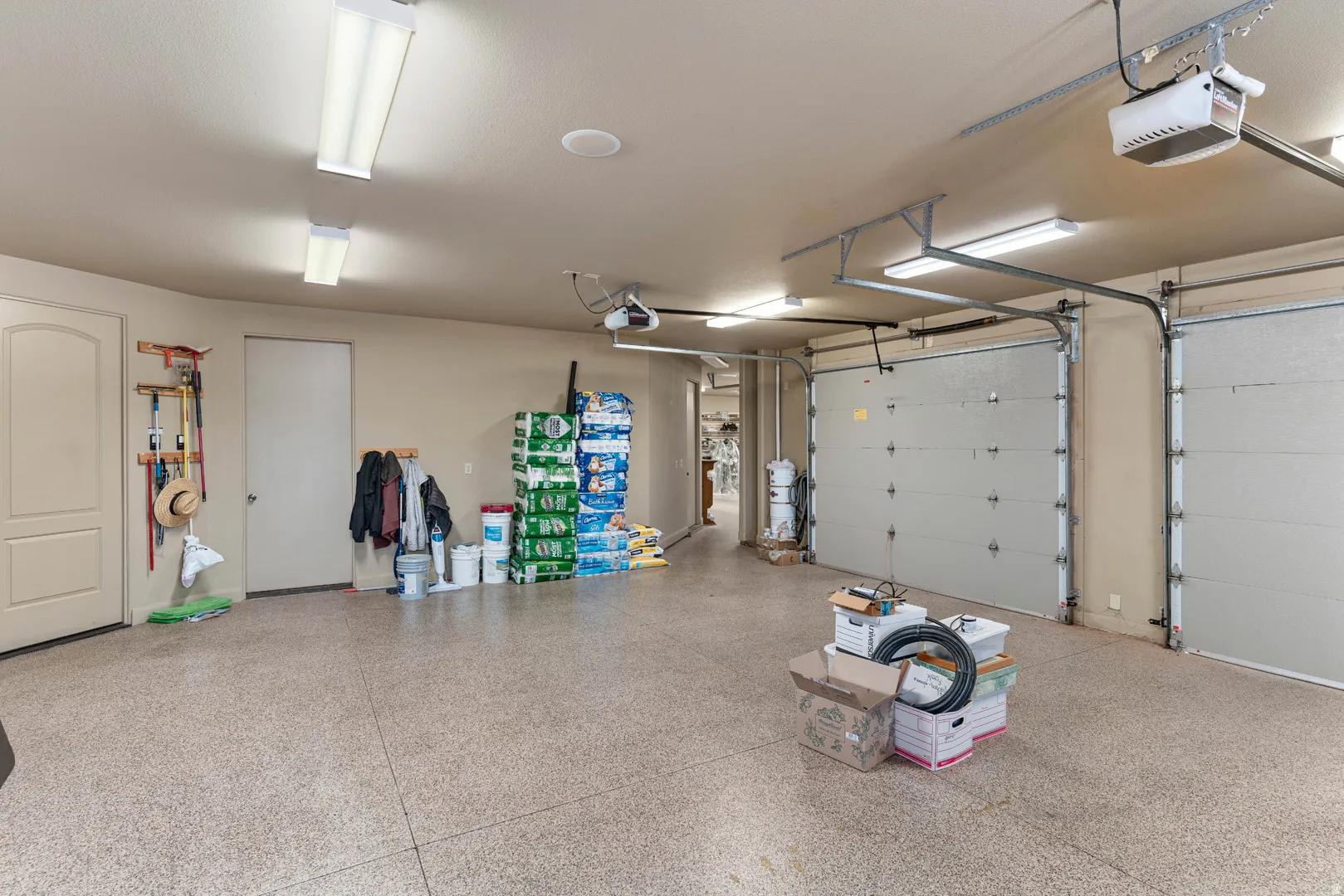 Spacious garage featuring two overhead doors, a speckled epoxy floor finish, multiple fluorescent light fixtures, a garage door opener, and interior access doors