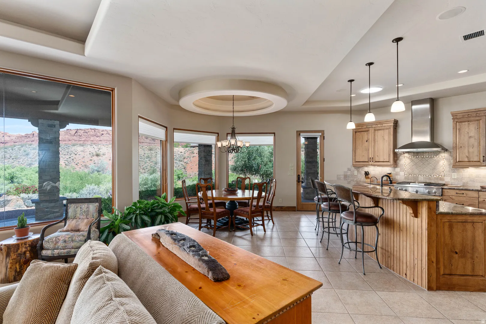 Open-concept living area featuring a kitchen with wood cabinetry, a range hood, and a breakfast bar, alongside a dining area with a circular tray ceiling and ample natural light from multiple windows