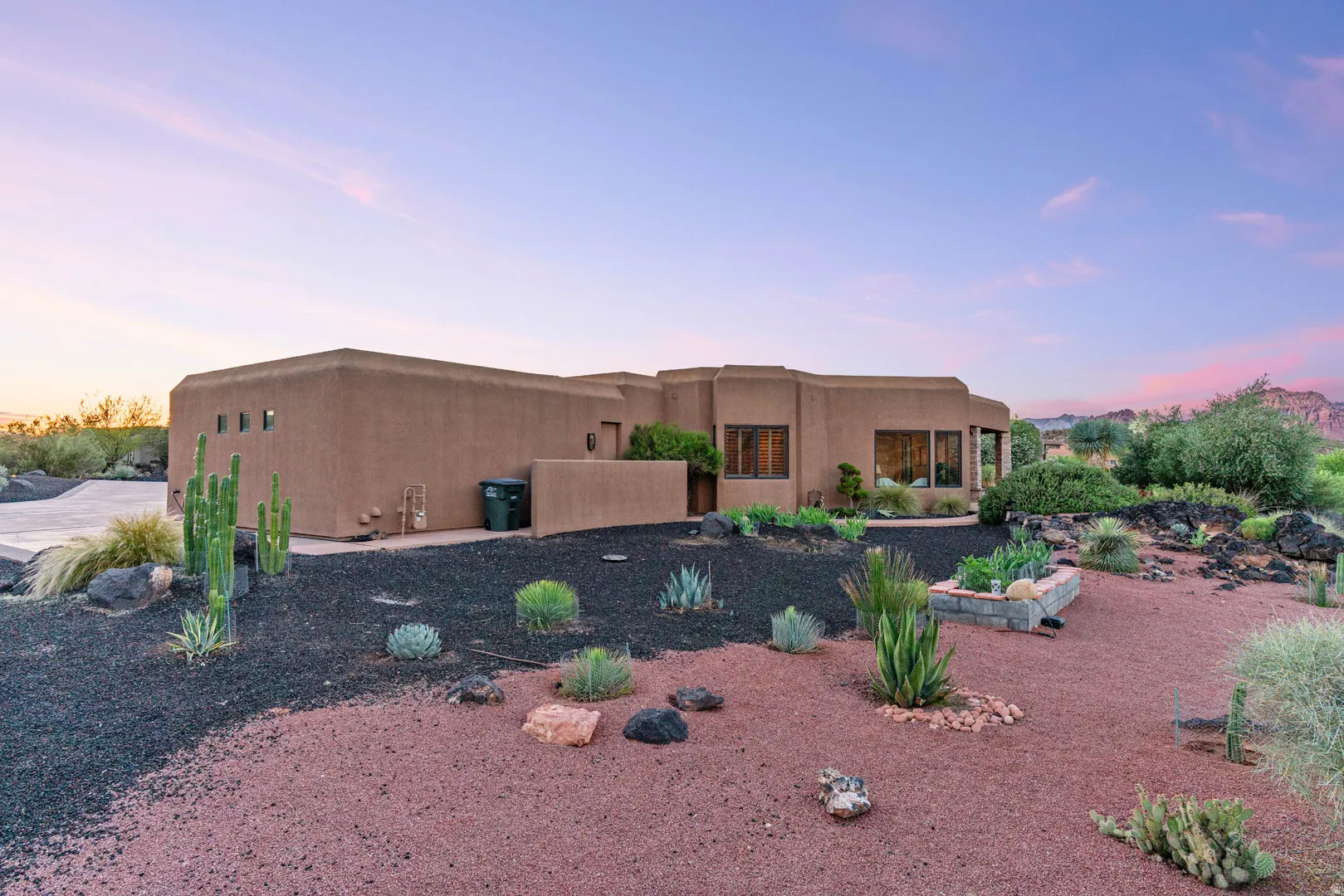 Southwestern-style architecture featuring stucco exterior, large windows, desert landscaping, raised garden bed, and a concrete driveway