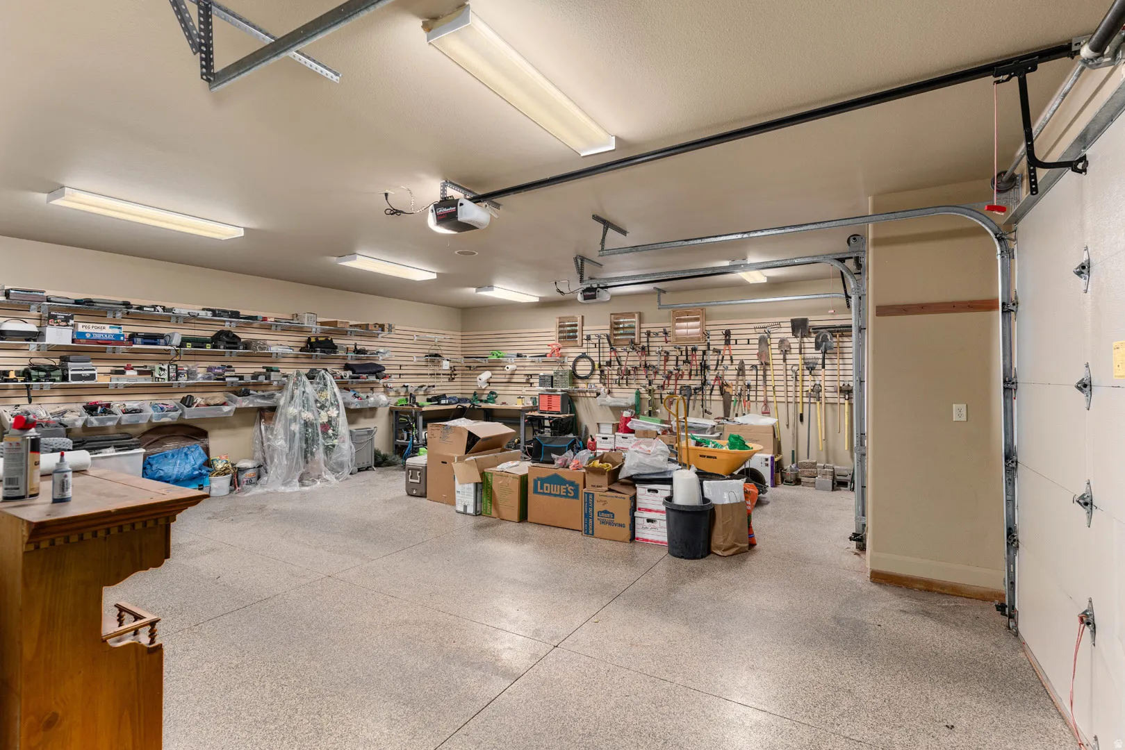 Spacious garage featuring a durable epoxy floor coating, multiple fluorescent light fixtures, overhead door track system, and extensive slat wall storage