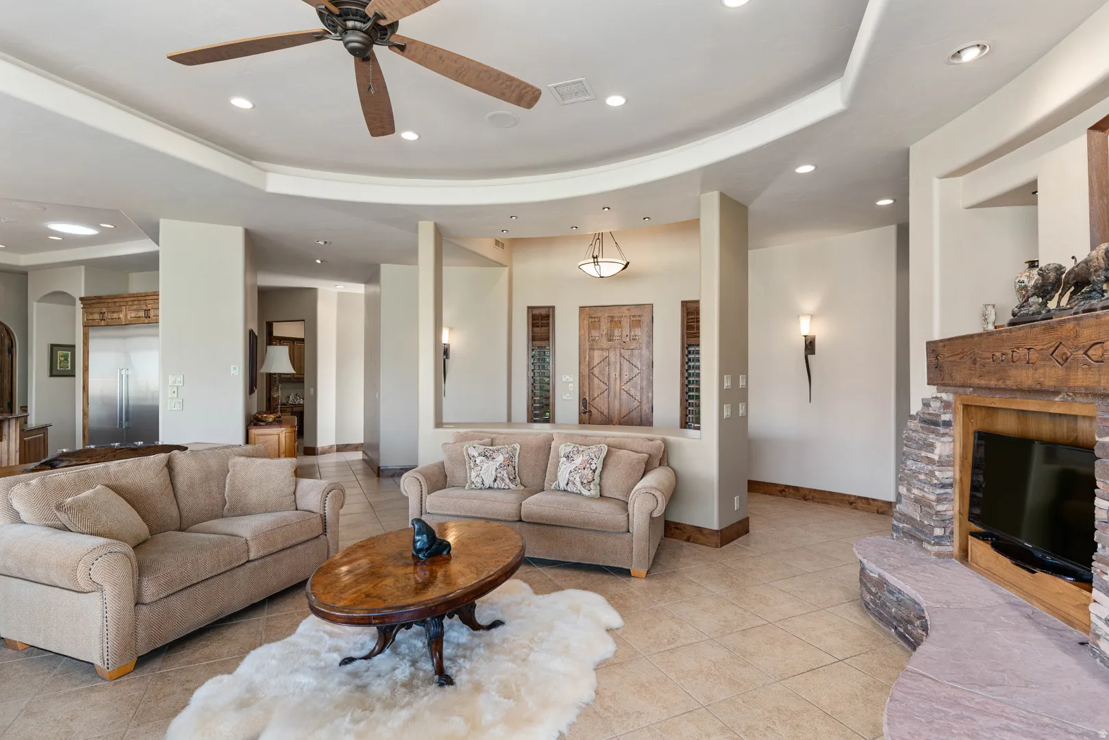 Spacious living area featuring tile flooring, a recessed ceiling with integrated lighting, and a ceiling fan