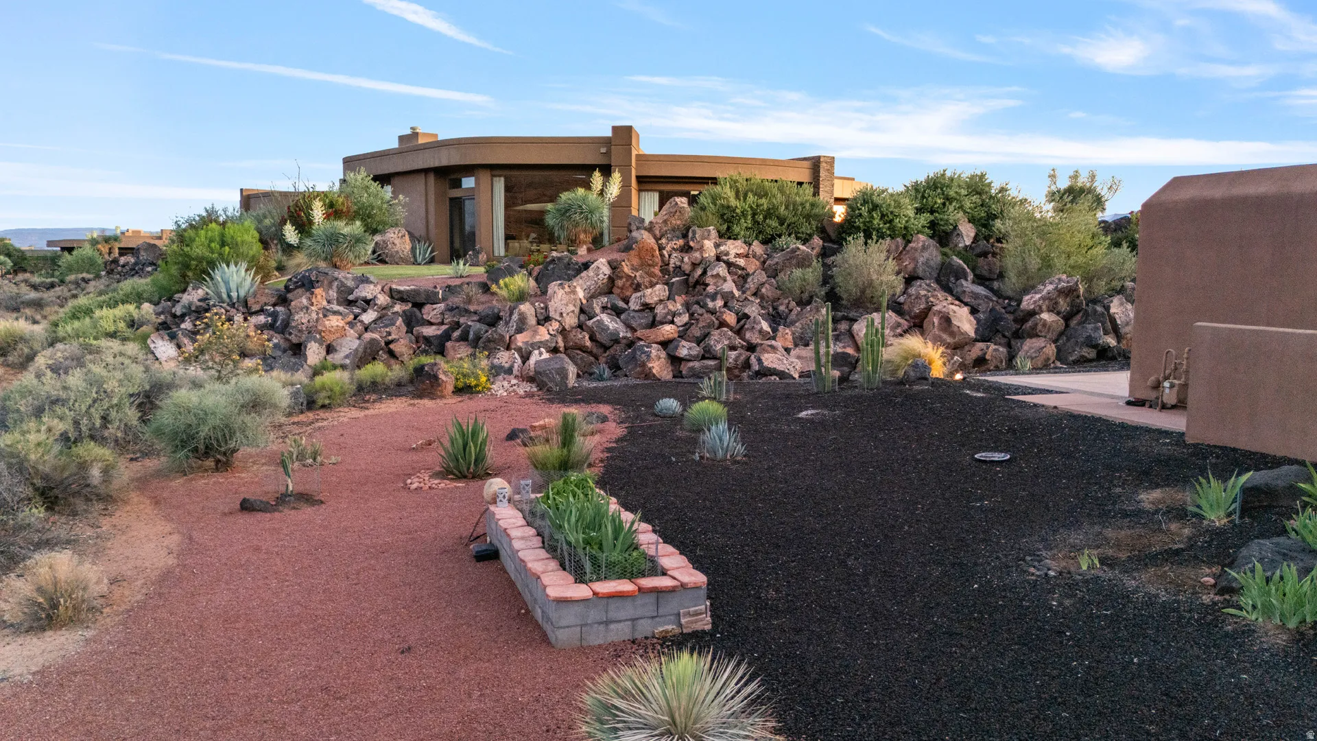 Desert landscaping featuring red and black gravel beds, diverse succulents, and natural rock formations