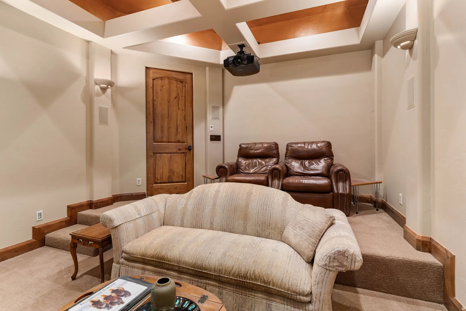 Dedicated media room featuring a coffered ceiling with wood-finish panels, a ceiling-mounted projector, and built-in wall speakers