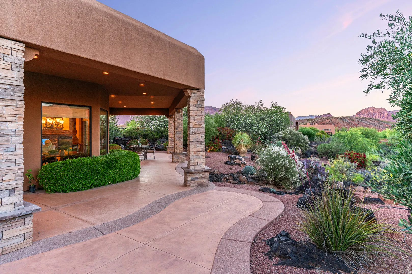 Covered outdoor patio featuring stone-clad pillars, recessed lighting, and a textured concrete surface with a decorative stone inlay