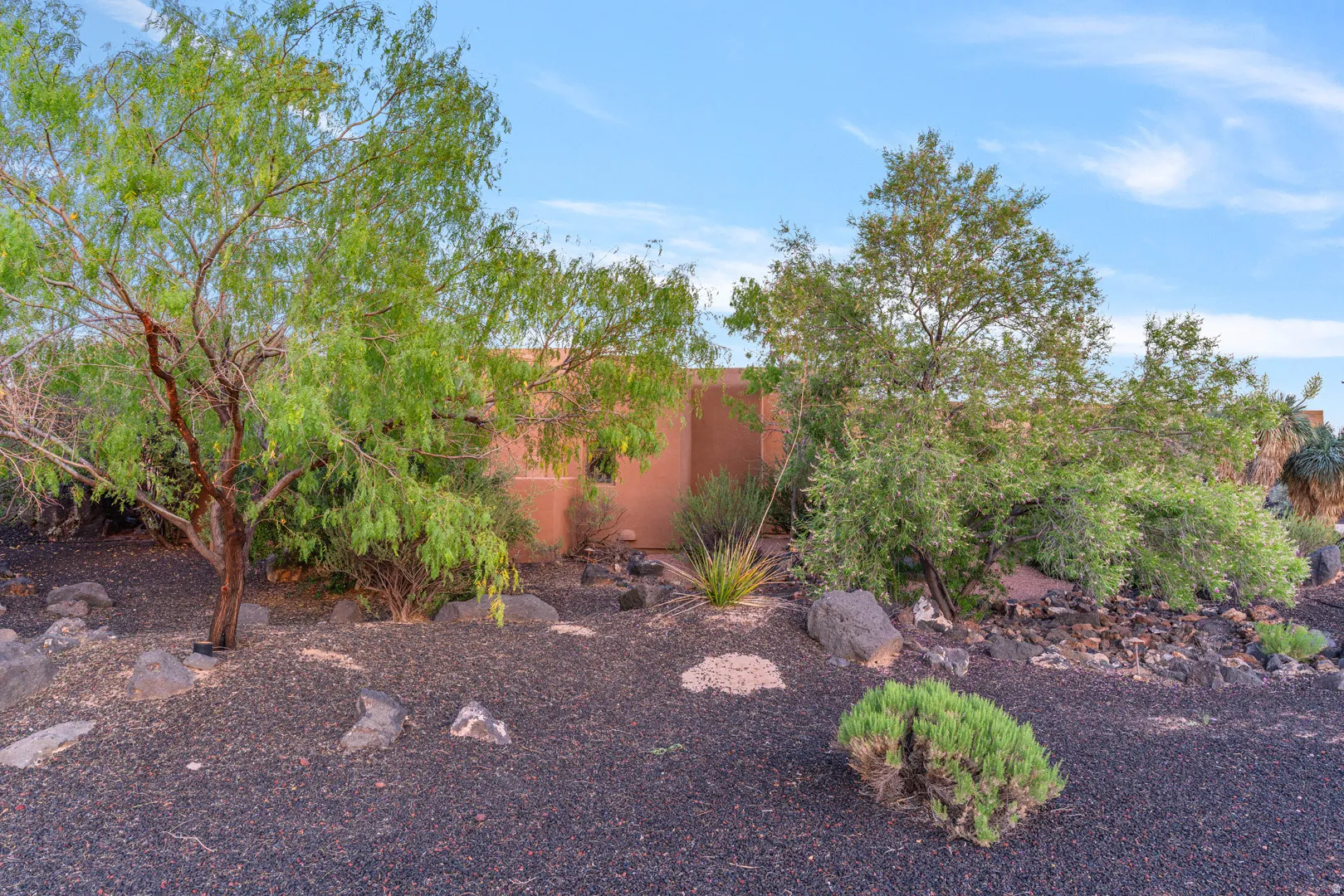 Desert landscaping featuring black lava rock, mature trees, and natural stone accents