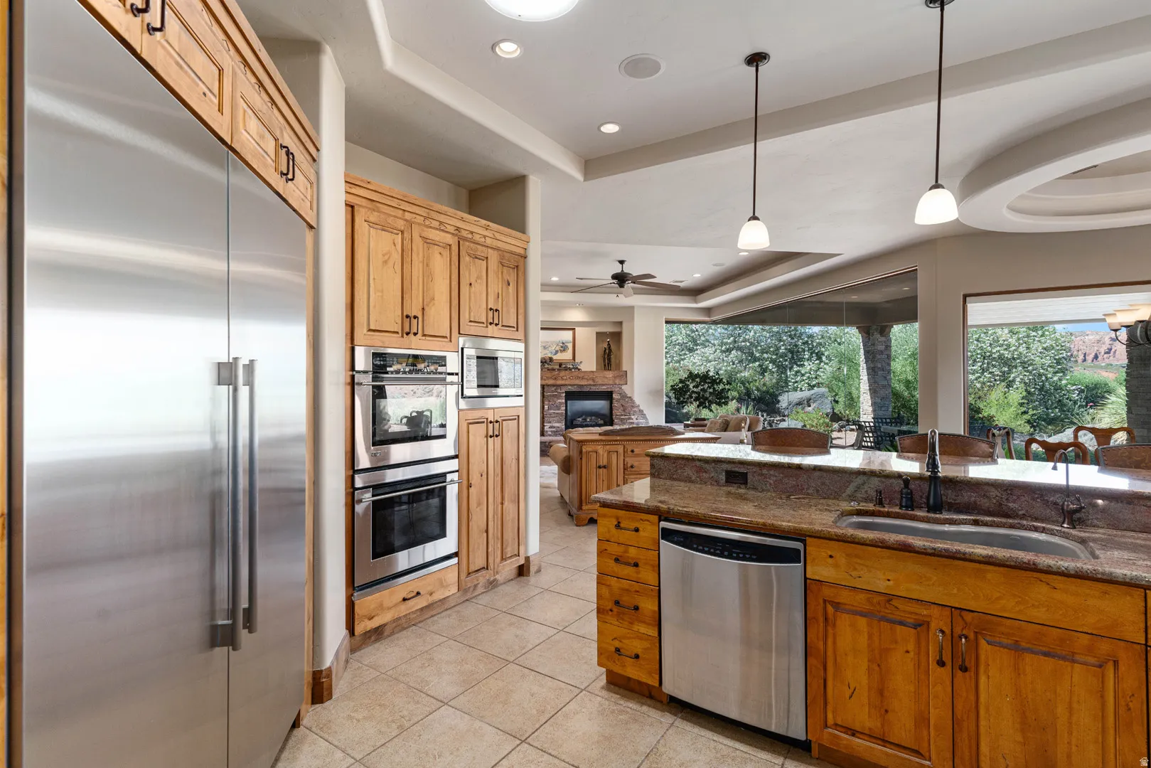 Gourmet kitchen featuring a large stainless steel refrigerator, double wall ovens, built-in microwave, stone countertops, and a kitchen island with sink and dishwasher