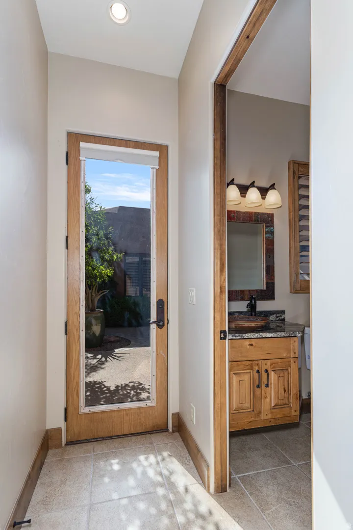 Recessed ceiling lighting illuminates a full-light wooden door with a dark handle, opening to an exterior patio