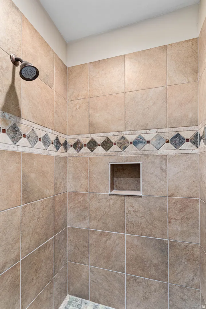 Shower featuring natural-toned wall tiling, decorative mosaic tile band, recessed niche, and a bronze-finish shower head