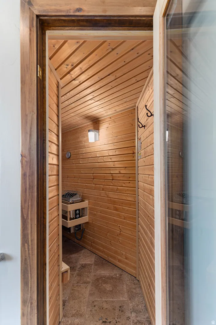 Custom sauna in primary bathroom featuring light wood paneling, a stone tile floor, and a built-in heating unit