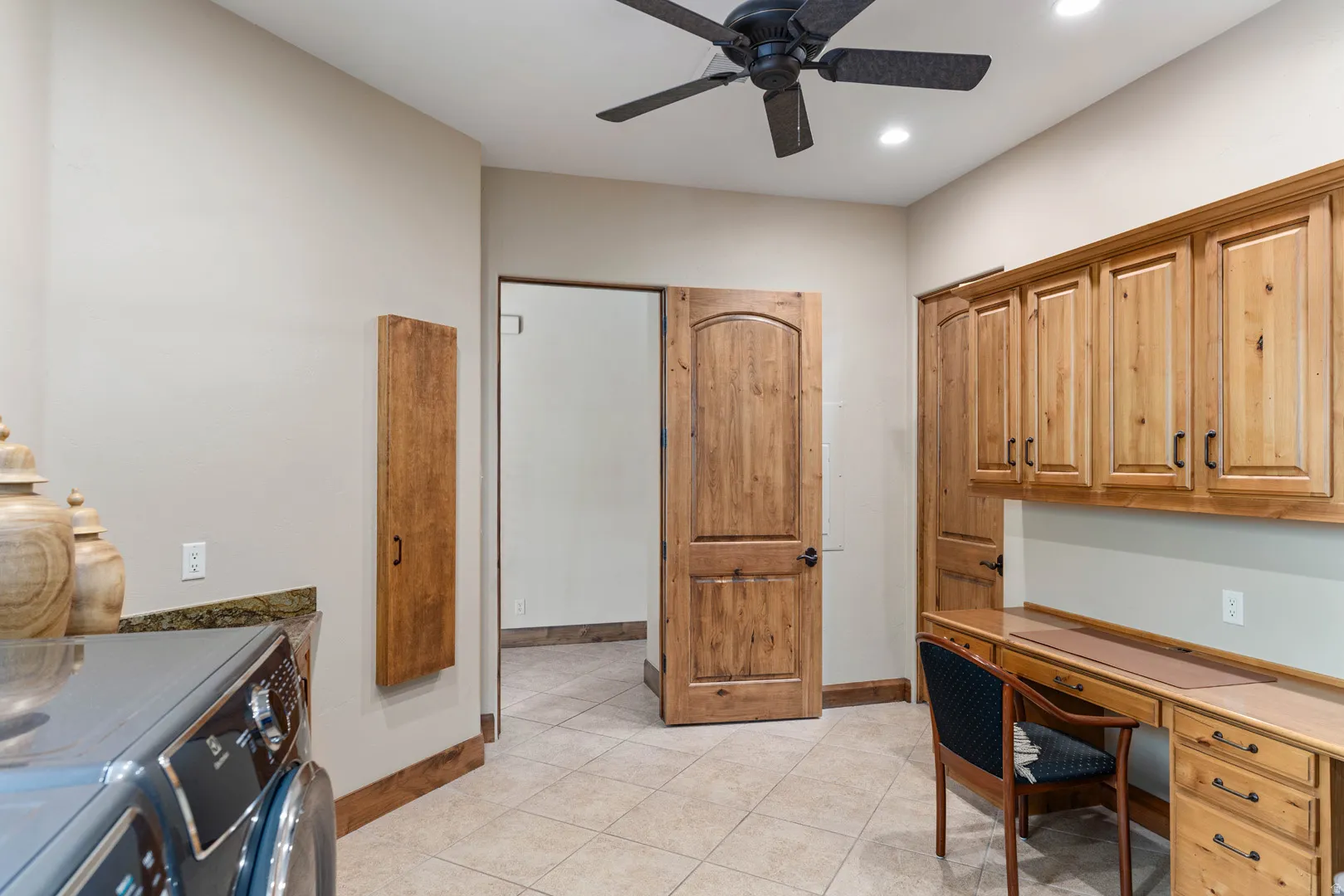 Functional utility room featuring wood-finish cabinetry, an integrated desk area, ceiling fan with lighting, recessed lighting, and tile flooring