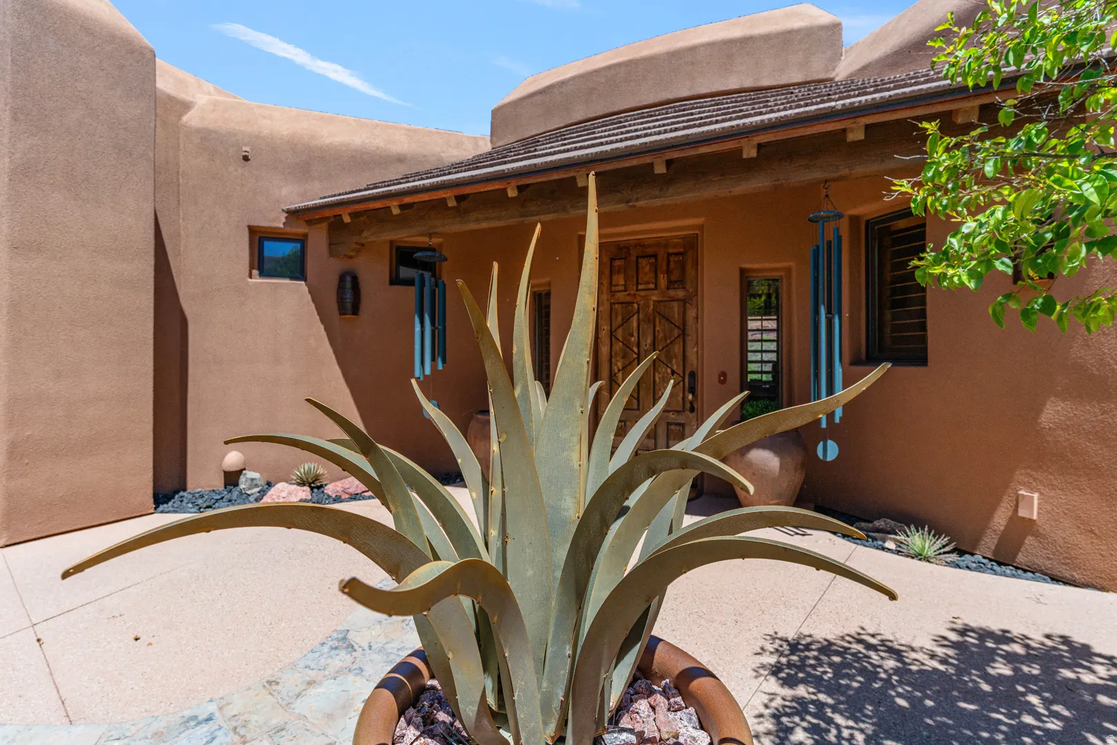Stucco exterior featuring a wood entry door with carved details, a covered entryway with exposed wood beams, and a tiled roofline