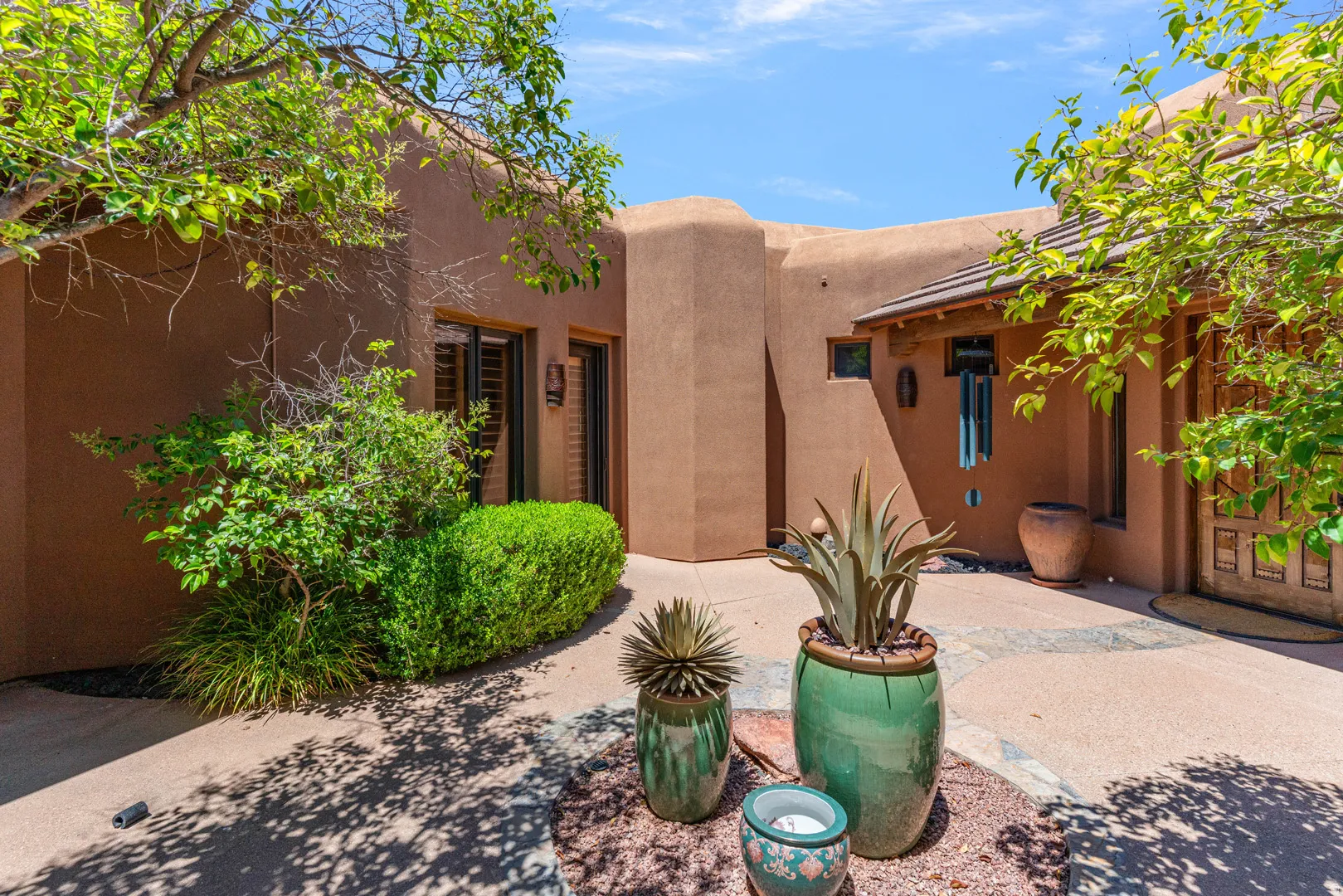 Stucco exterior architecture featuring a covered entry, mature landscaping, and a terracotta tile roof accent