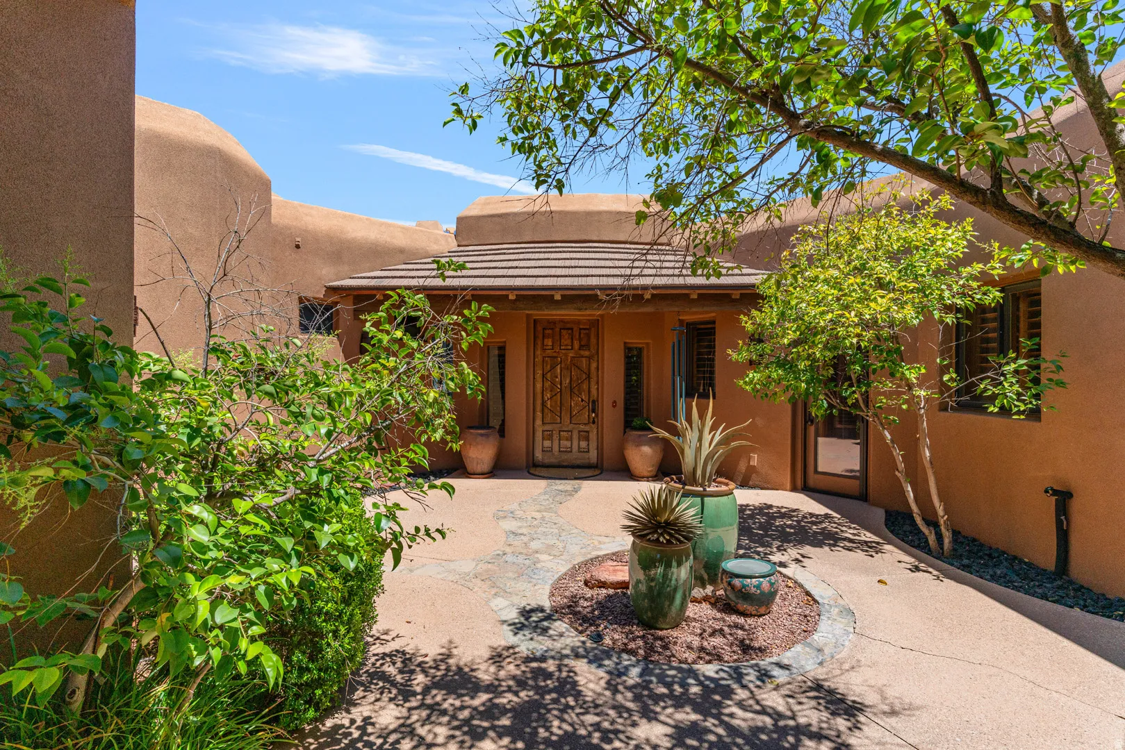 Courtyard entry featuring a custom wooden door, tile roof, stucco exterior, and mature landscaping
