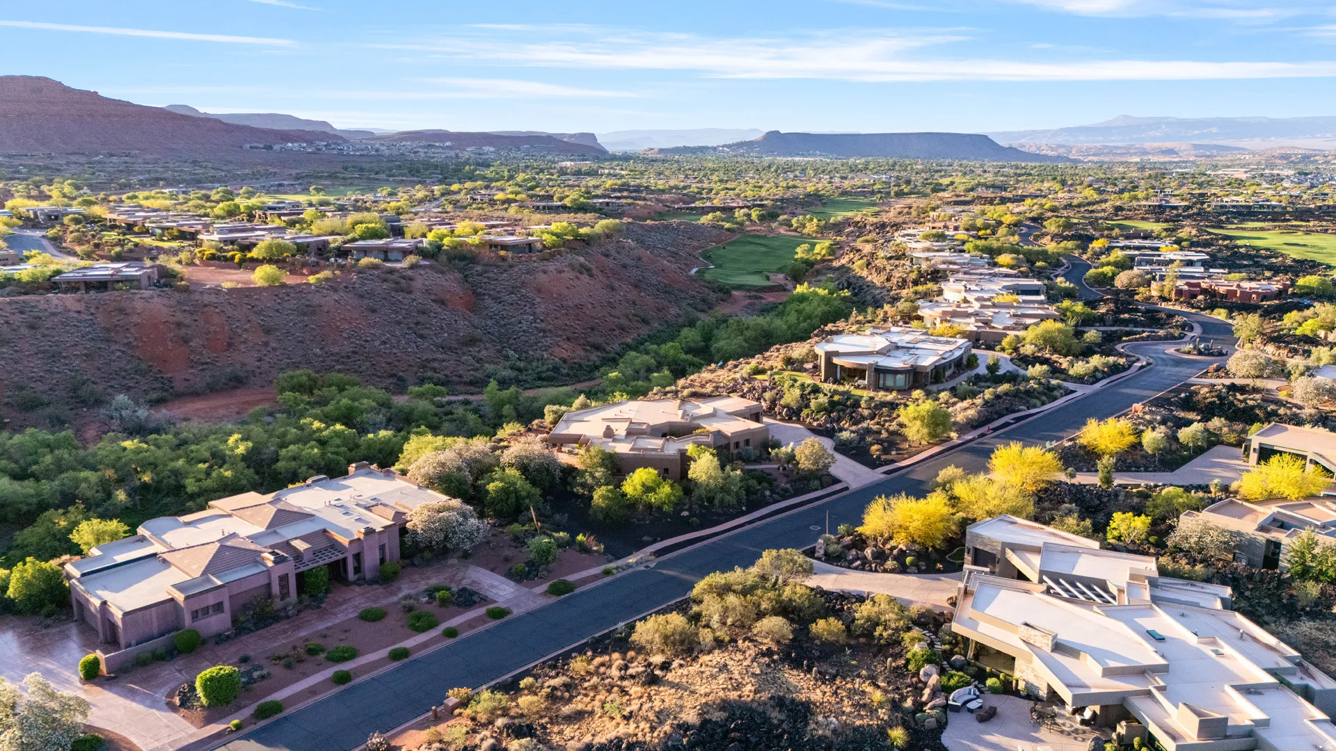 Expansive residential landscape featuring a paved roadway, red rock formations, and mature desert flora