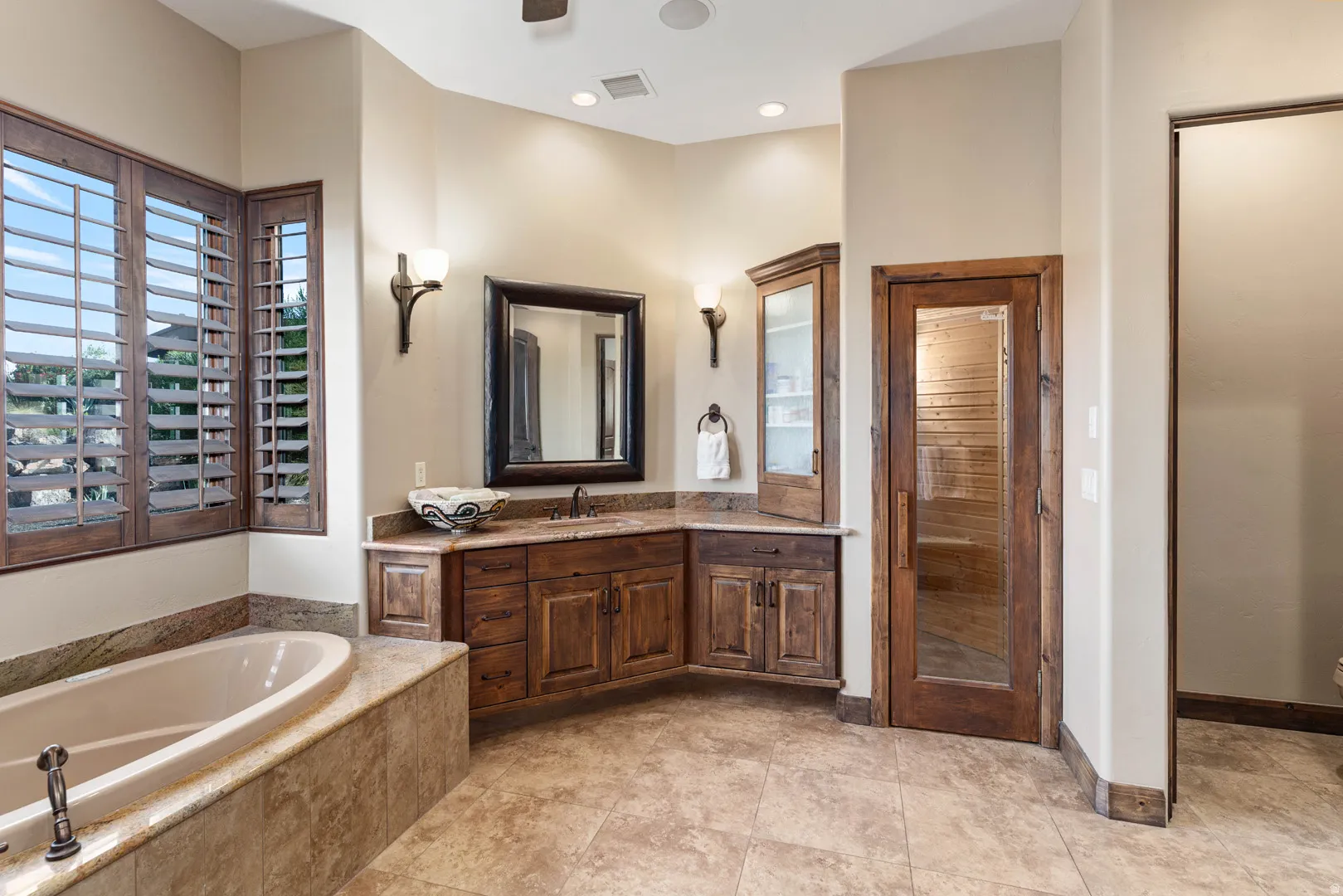 Bathroom featuring a built-in soaking tub with stone surround, custom wood vanity with stone countertop, and a glass-paneled wood door