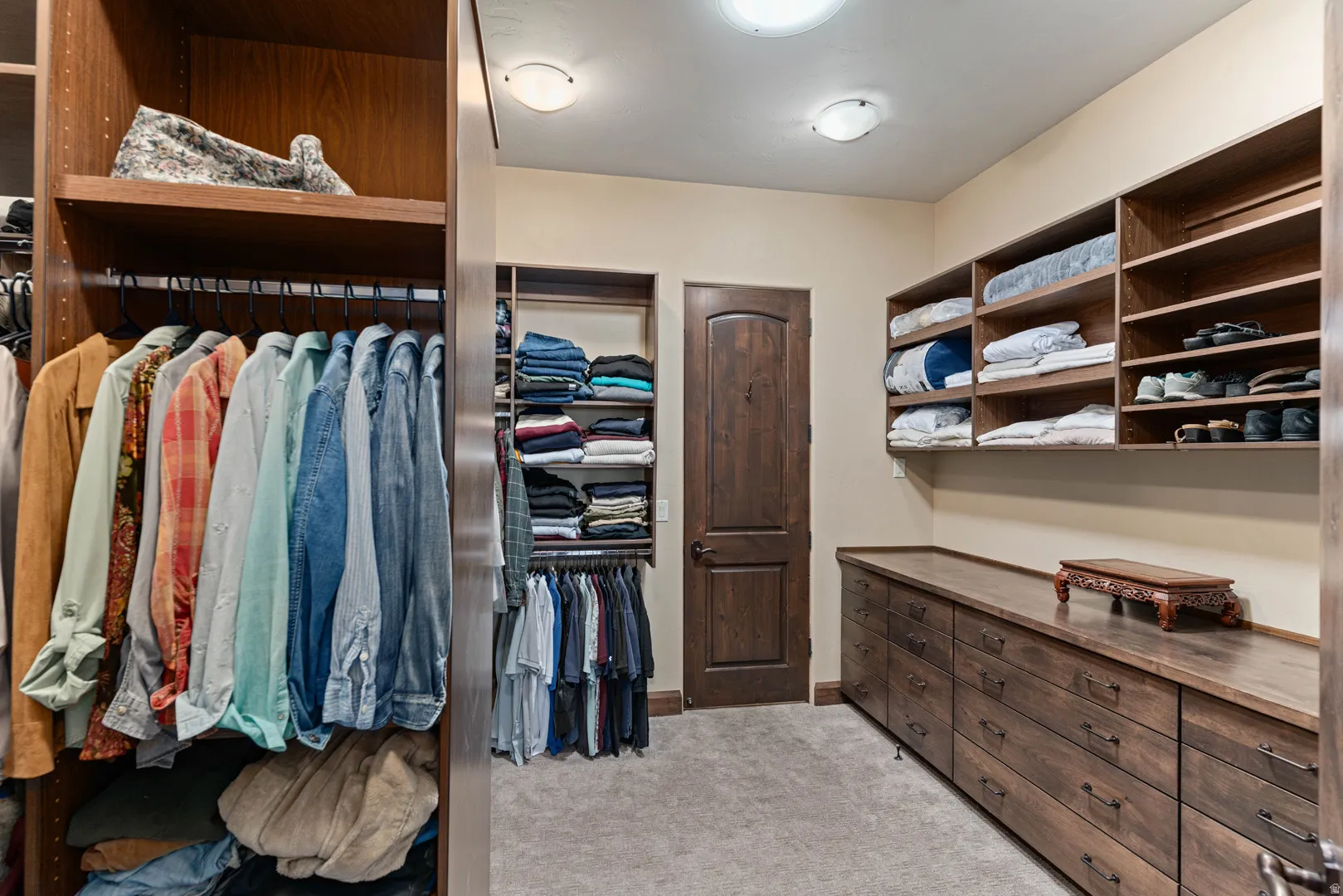 Spacious prmary custom closet featuring extensive wood-finish cabinetry, built-in shelving, multiple hanging rods, and a solid wood-finish door