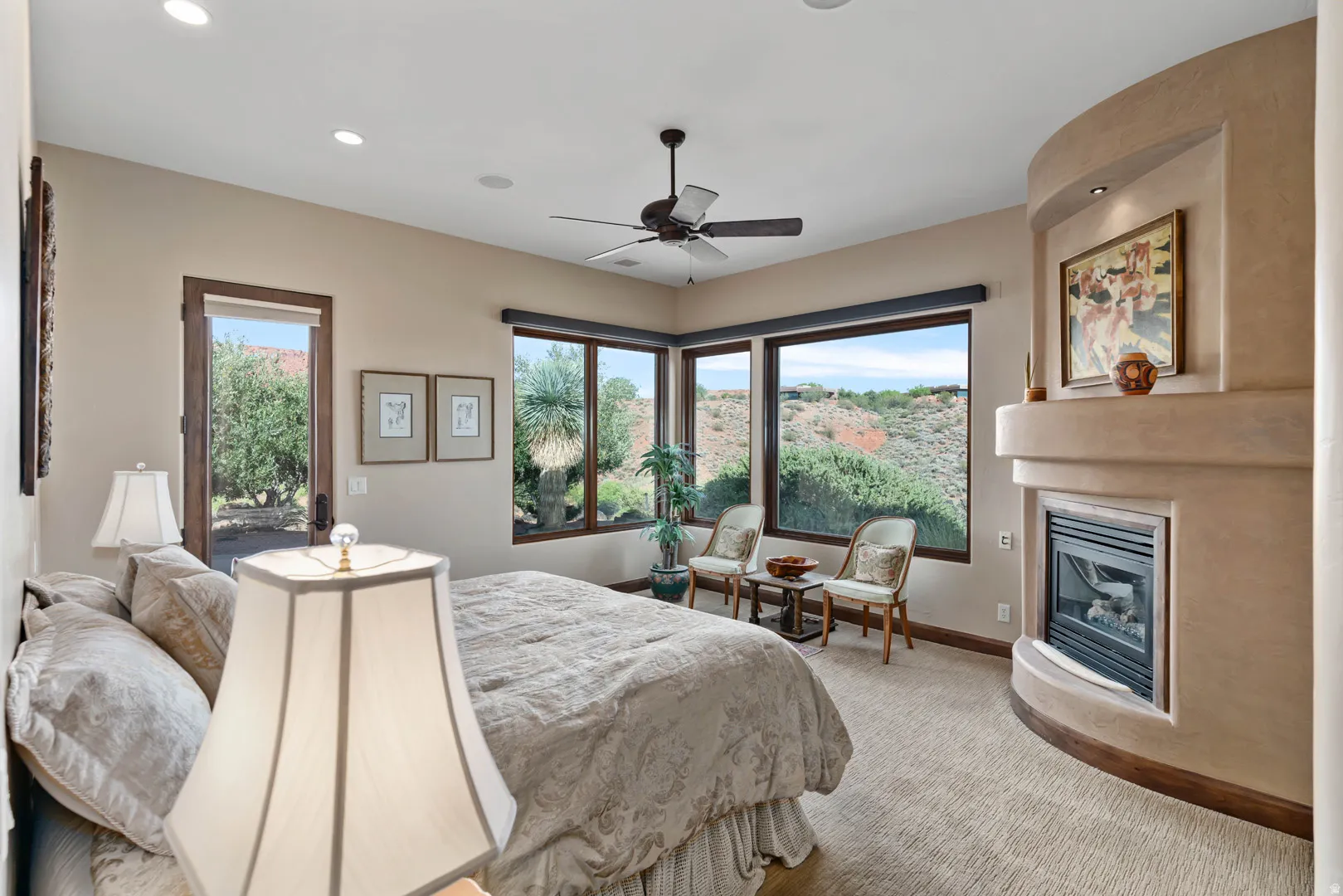 Primary bedroom with curved fireplace feature with a gas insert, large picture windows, recessed lighting, ceiling fan, and a wood-trimmed exterior door
