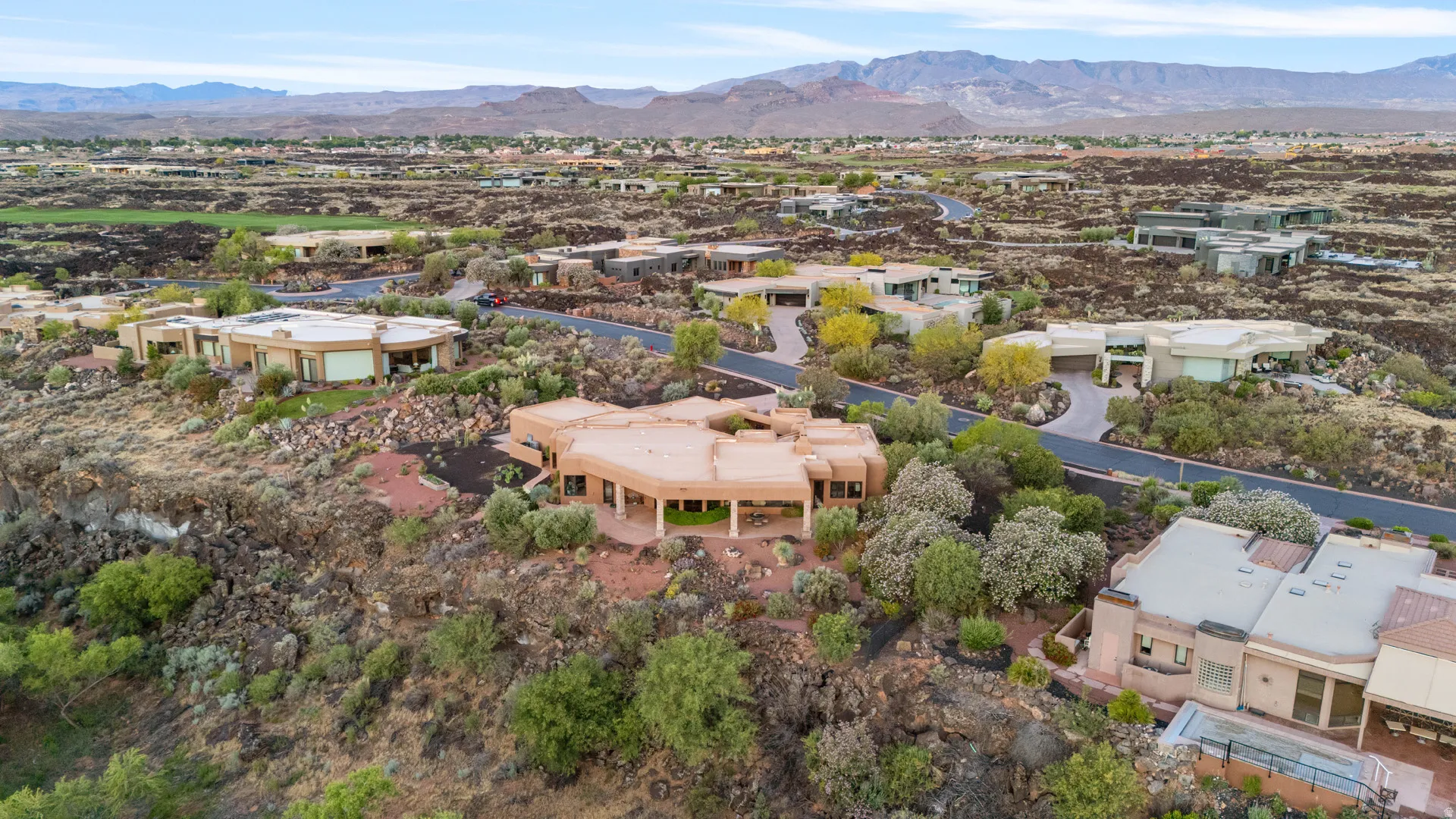 Desert Modern architecture featuring a terracotta-hued exterior, a multi-level design, a covered patio, and xeriscaped grounds with native plantings, all set against a backdrop of distant mountains