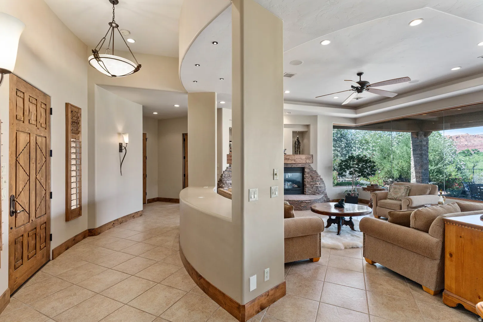 Spacious living area featuring tile flooring, a stone-faced fireplace, and a tray ceiling with recessed lighting