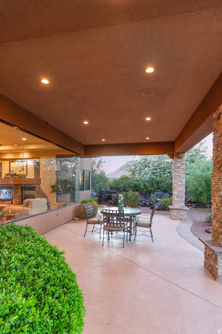 Expansive covered patio featuring recessed lighting, a stone-clad pillar, and a curved concrete patio surface bordered by gravel and shrubbery