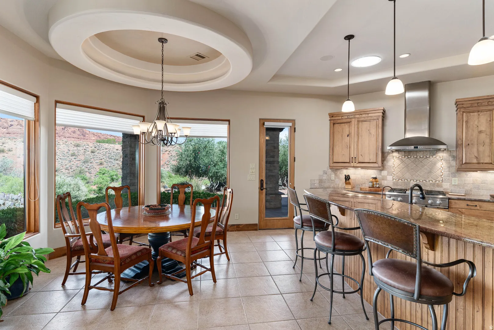 Open-concept kitchen and dining area featuring a tiered circular tray ceiling with a chandelier, tile flooring, a kitchen island with seating, and wood cabinetry with a tile backsplash