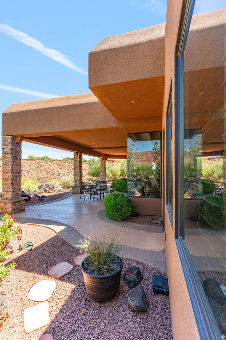 Stucco exterior featuring a covered patio with stone columns, large windows, and a landscaped rock garden with stepping stones