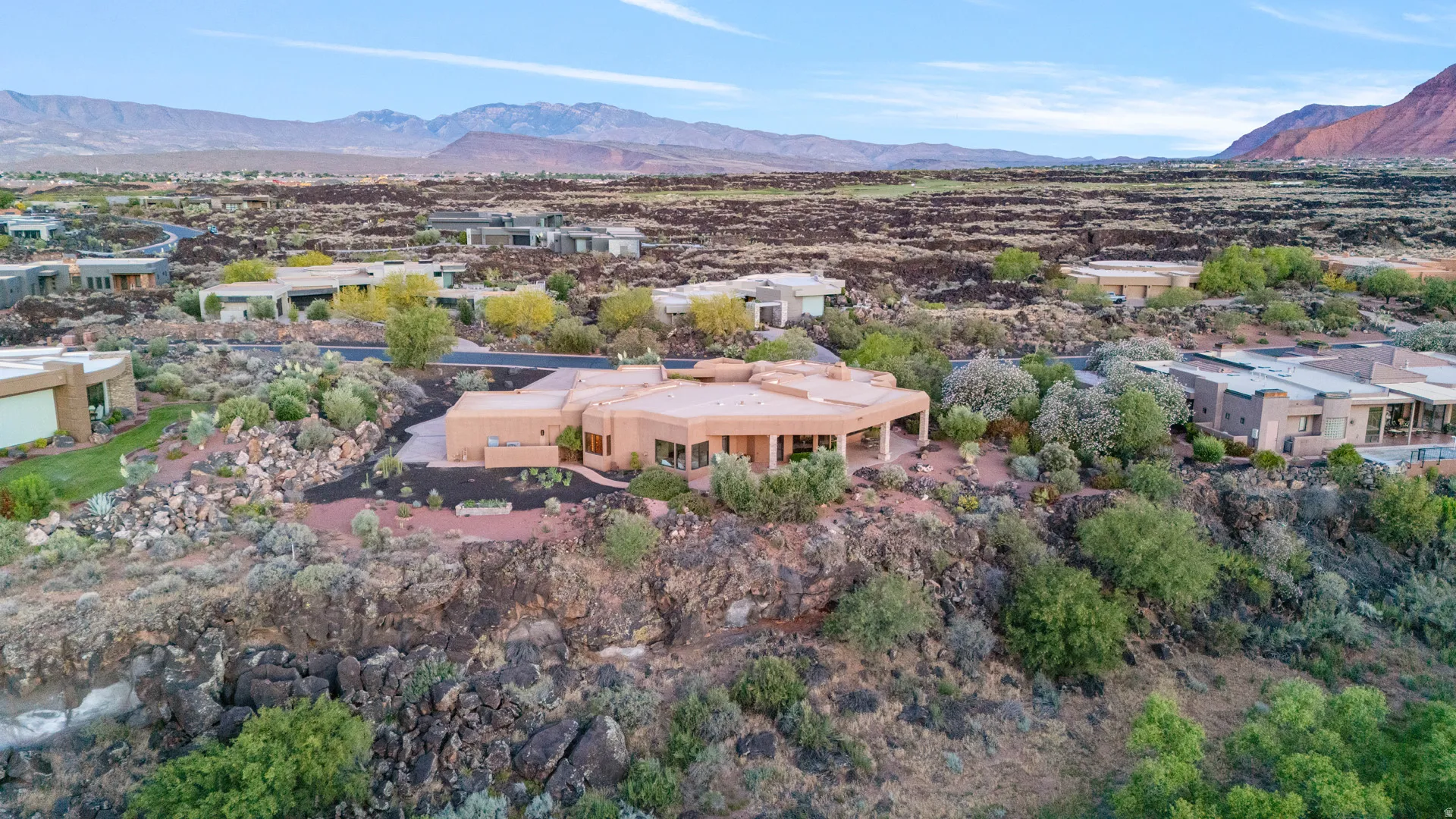 Desert landscape featuring a modern stucco residence with a curved patio, surrounded by natural rock formations and varied desert flora
