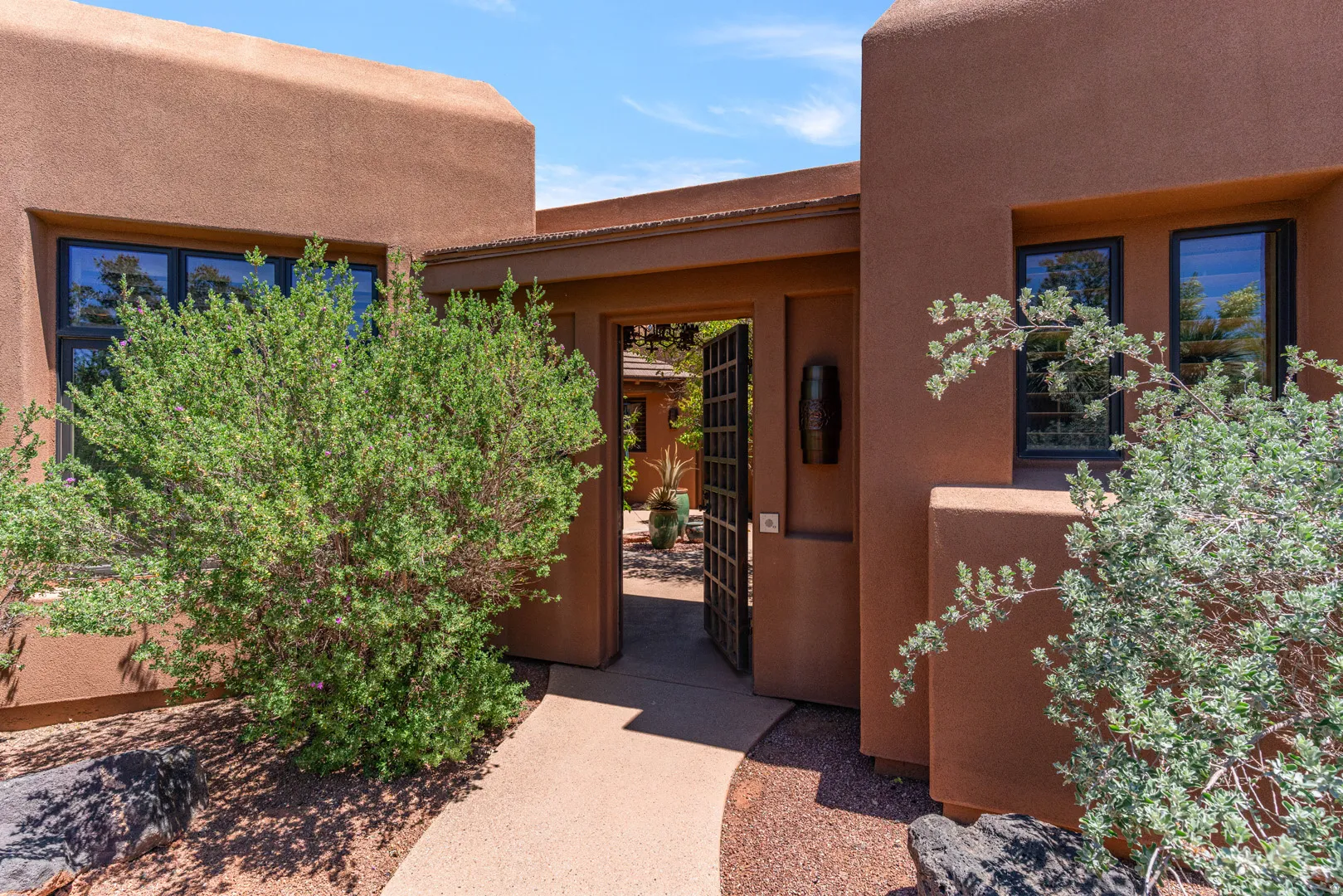 Stucco exterior with black-framed windows, a wrought iron gate, and a concrete pathway