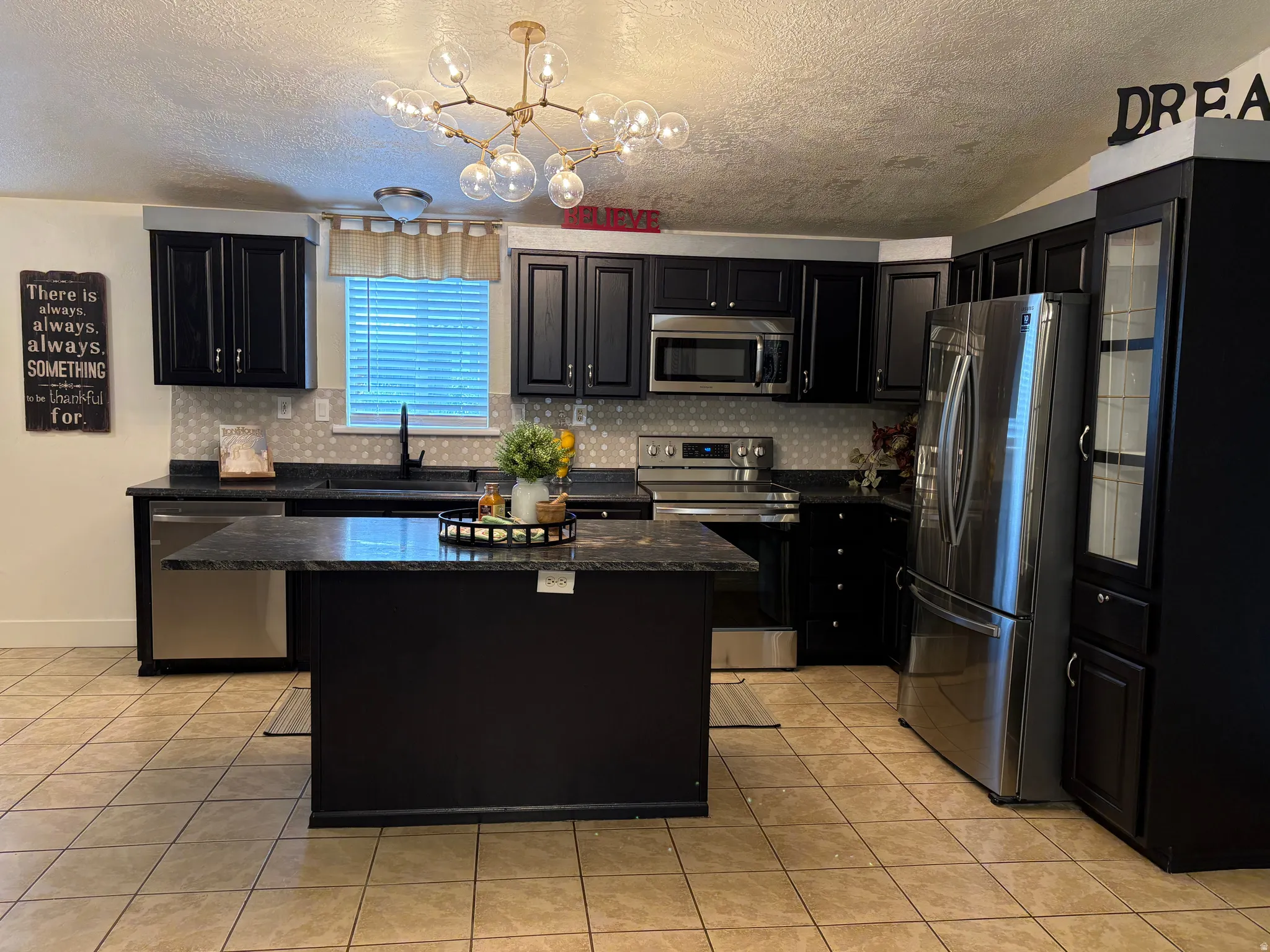 Modern kitchen featuring dark cabinetry, stone-finish countertops, stainless steel appliances, and a central island