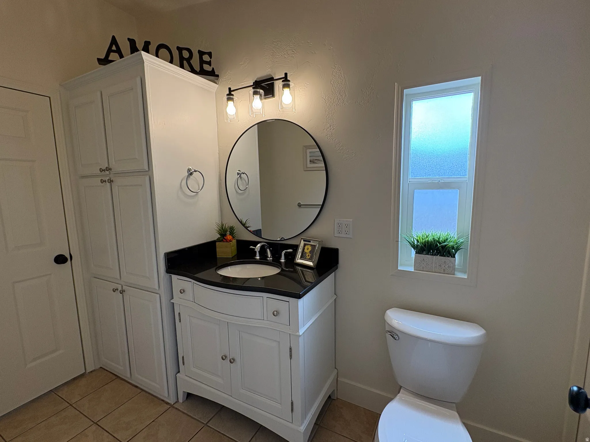 Bathroom featuring a white vanity with a black countertop, a circular mirror, and a three-light fixture