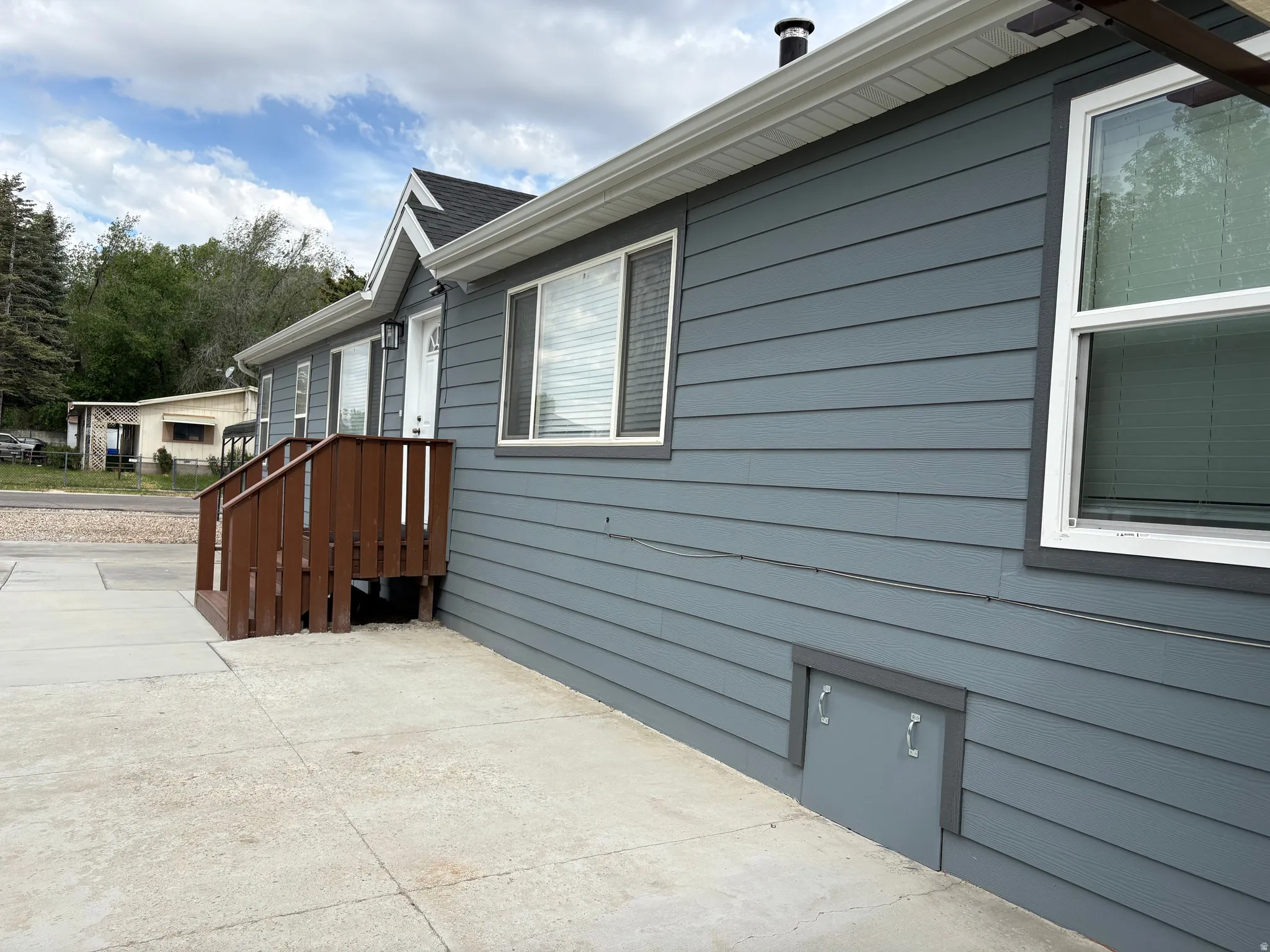 Exterior featuring horizontal siding, white trim, a brown wood-tone deck, and a concrete patio