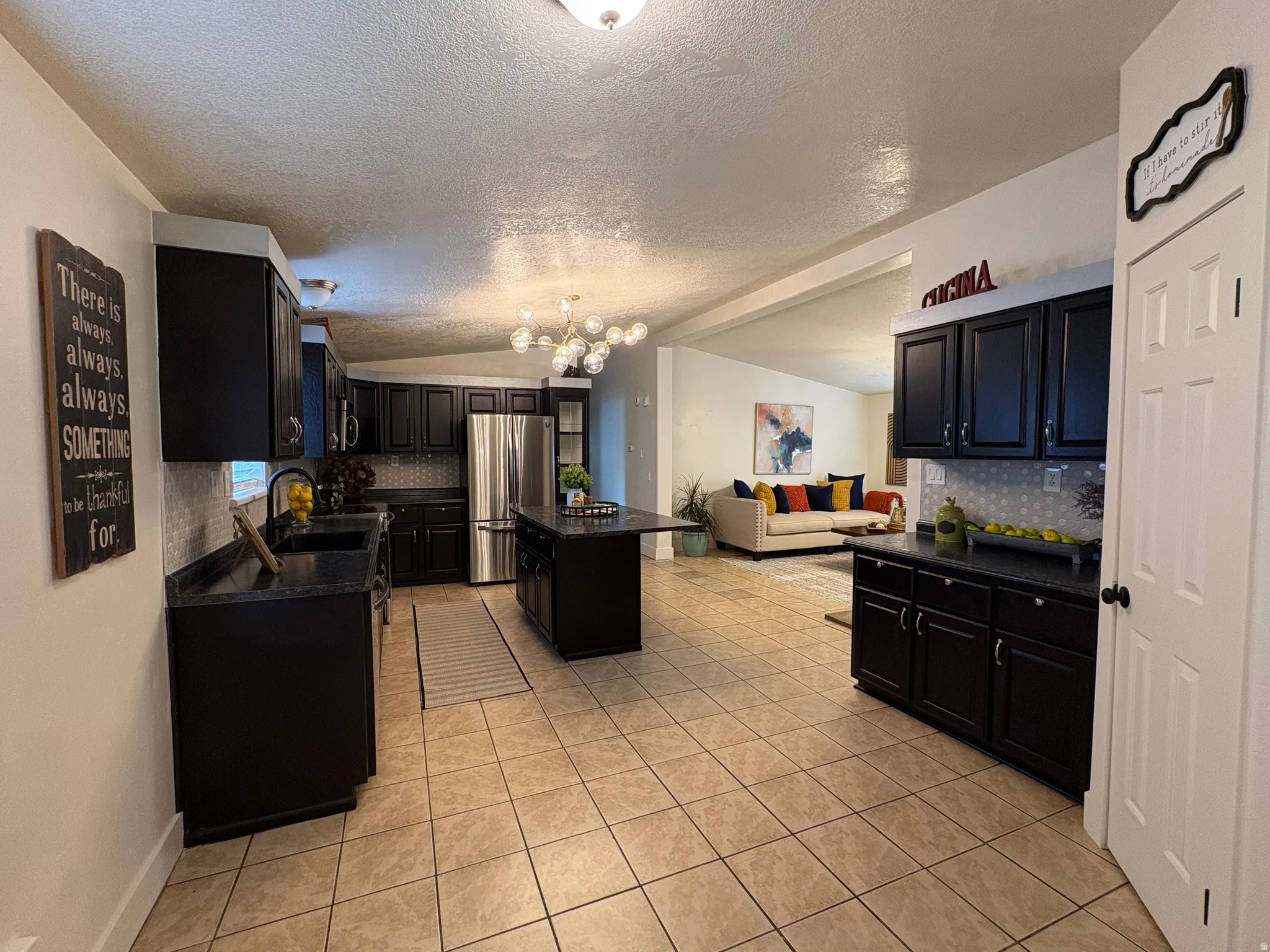 Open-concept kitchen featuring dark cabinetry, dark countertops, a center island, stainless steel refrigerator, and tile flooring