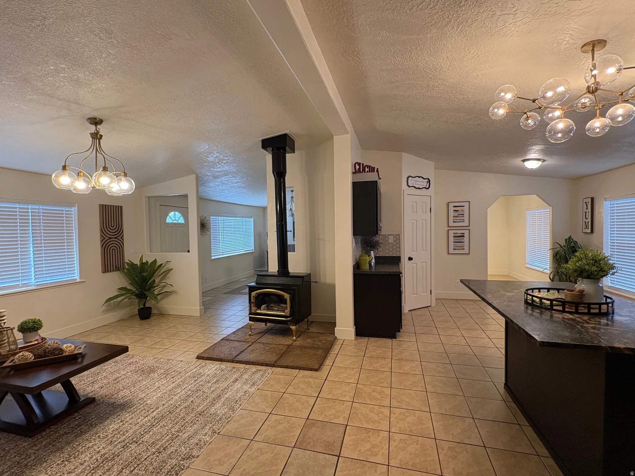Spacious interior featuring a central black wood-burning stove, tile flooring, and two distinct lighting fixtures