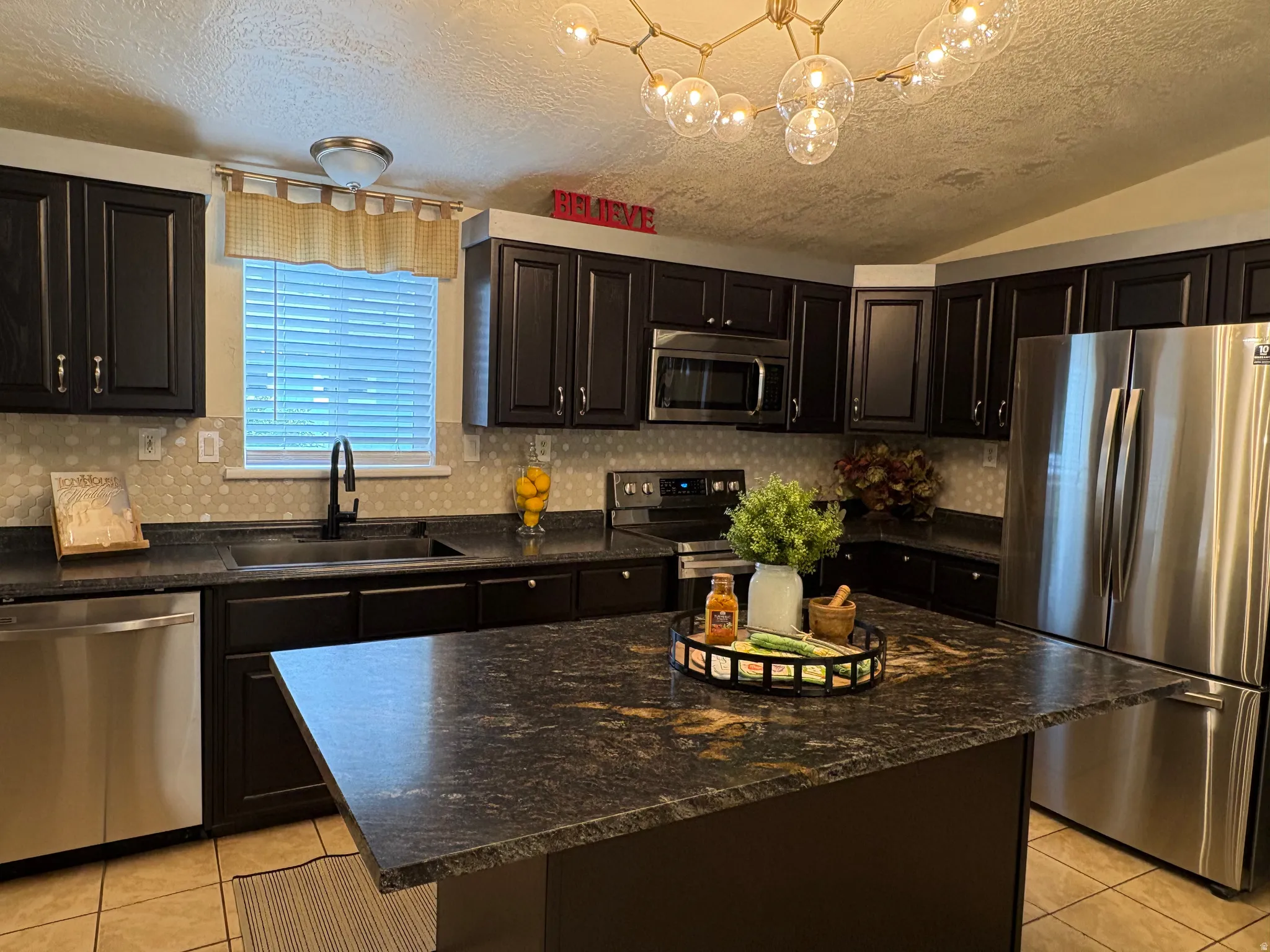 Kitchen featuring dark cabinetry with brushed nickel hardware, stainless steel appliances, and a central island with a contrasting countertop