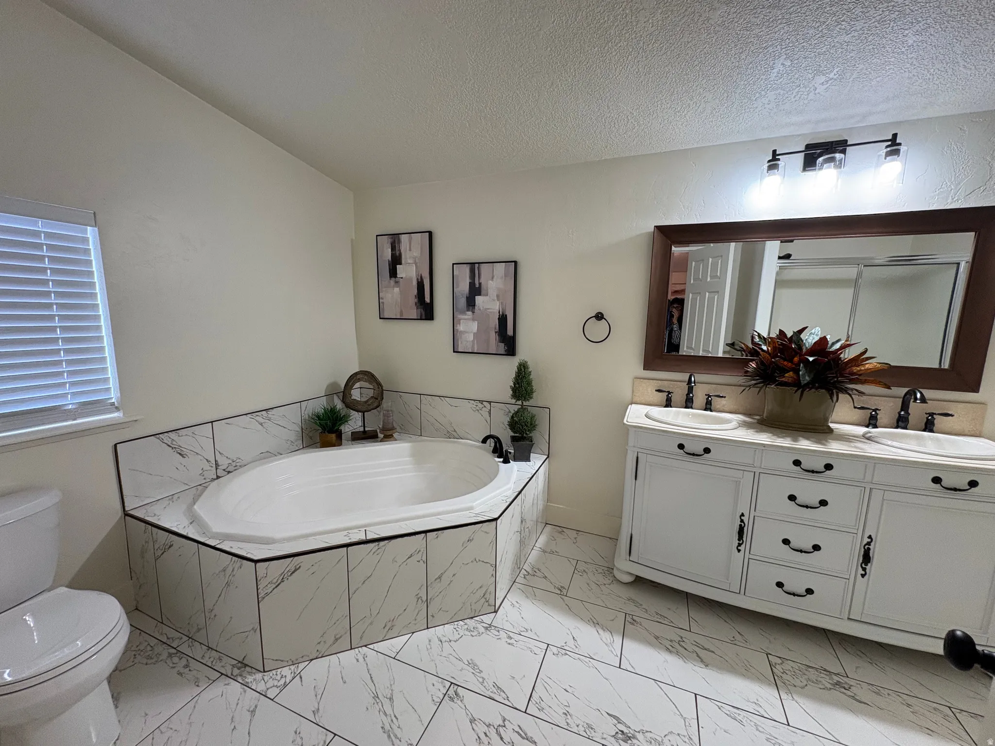 Bathroom featuring a corner soaking tub with marble-look tile surround and a double vanity with an integrated countertop and two undermount sinks