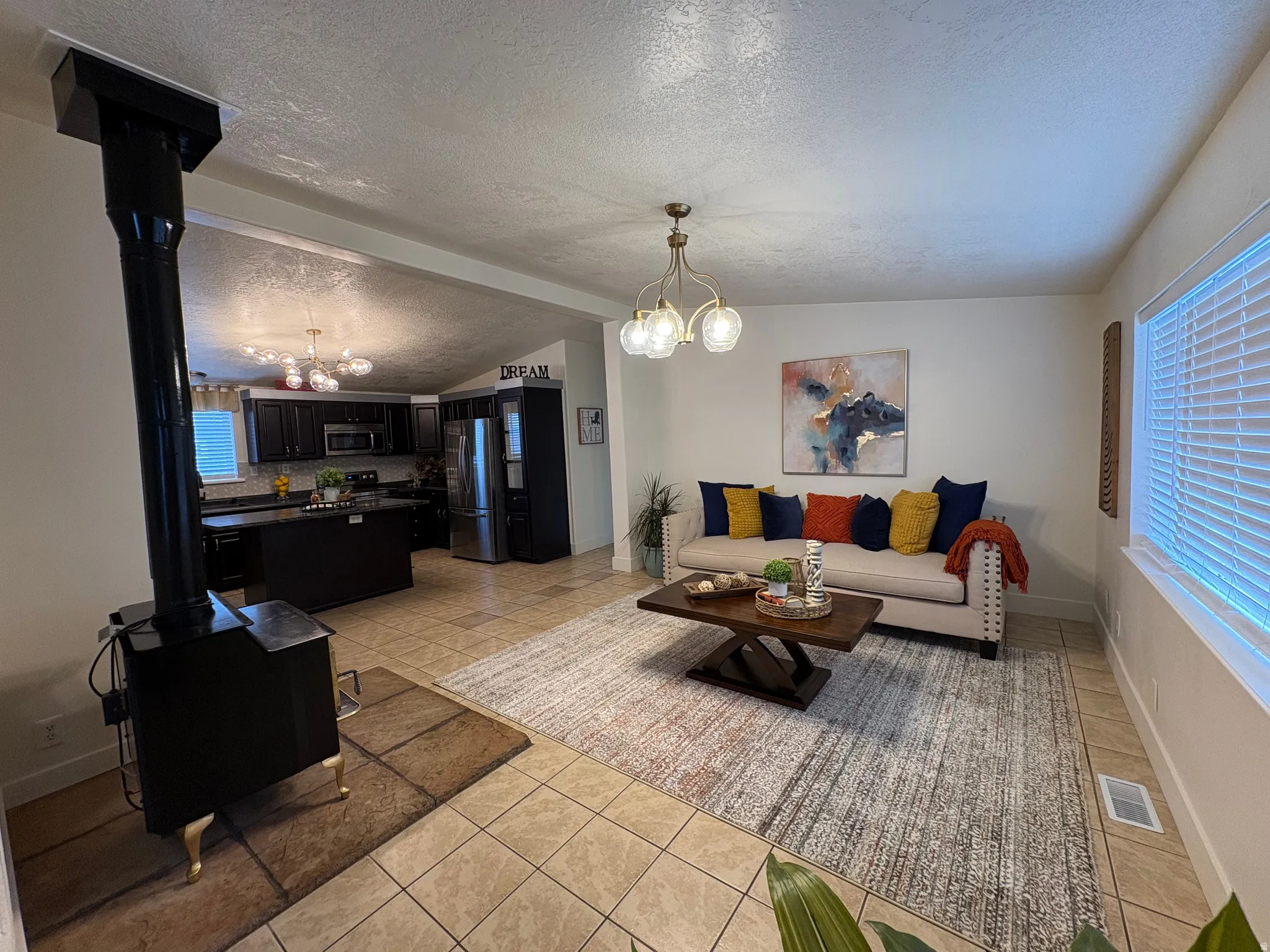 Open-concept living space featuring a black wood-burning stove, tile flooring, and a kitchen with dark cabinetry and stainless steel appliances