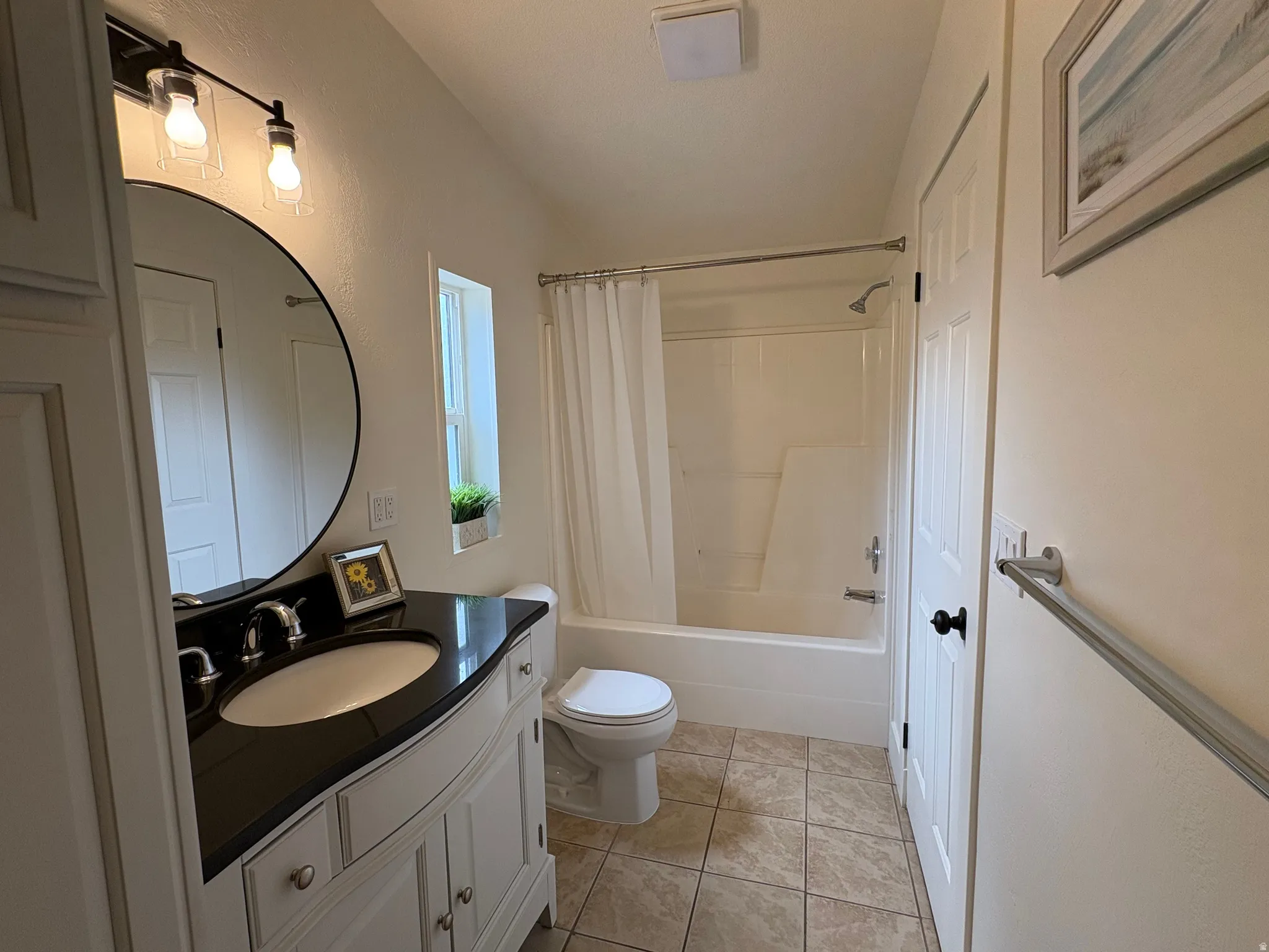 Bathroom featuring a white vanity with a dark countertop, an undermount sink, and a circular mirror
