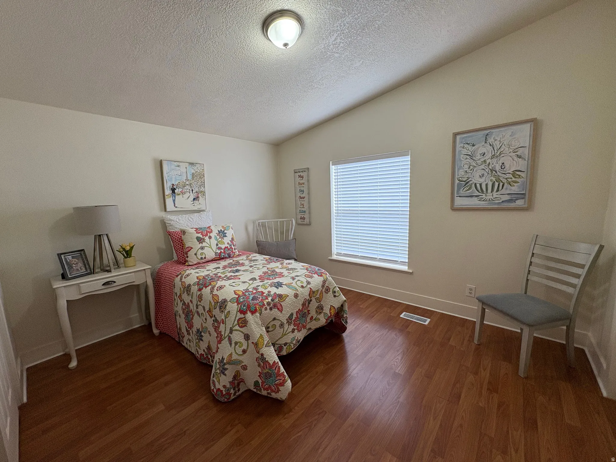 Vaulted ceiling room with wood-finish flooring, featuring a window with blinds, a ceiling-mounted light fixture, and white baseboards