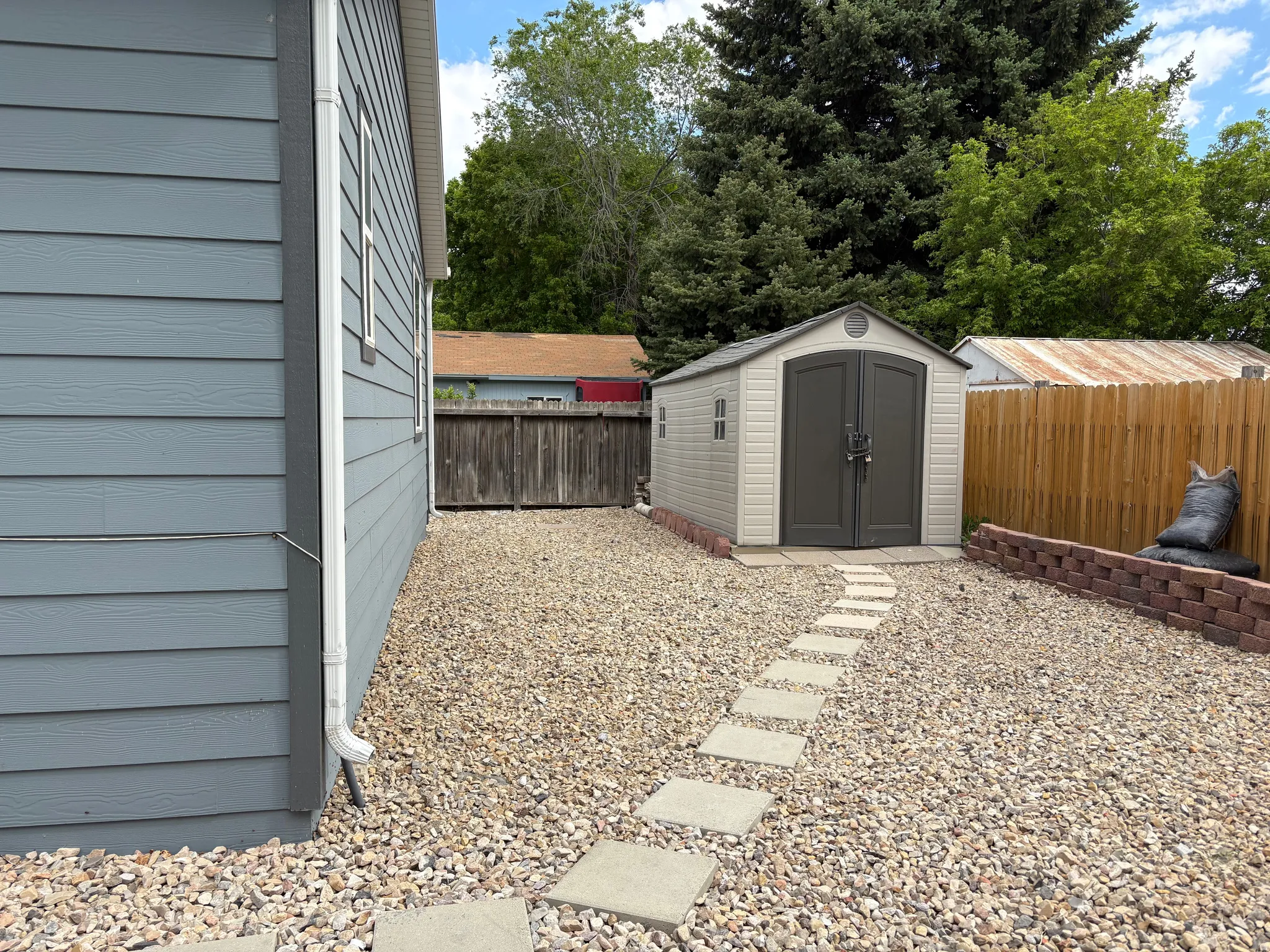 Gravel side yard featuring a storage shed with double doors, a concrete stepping stone path, and a brick retaining wall