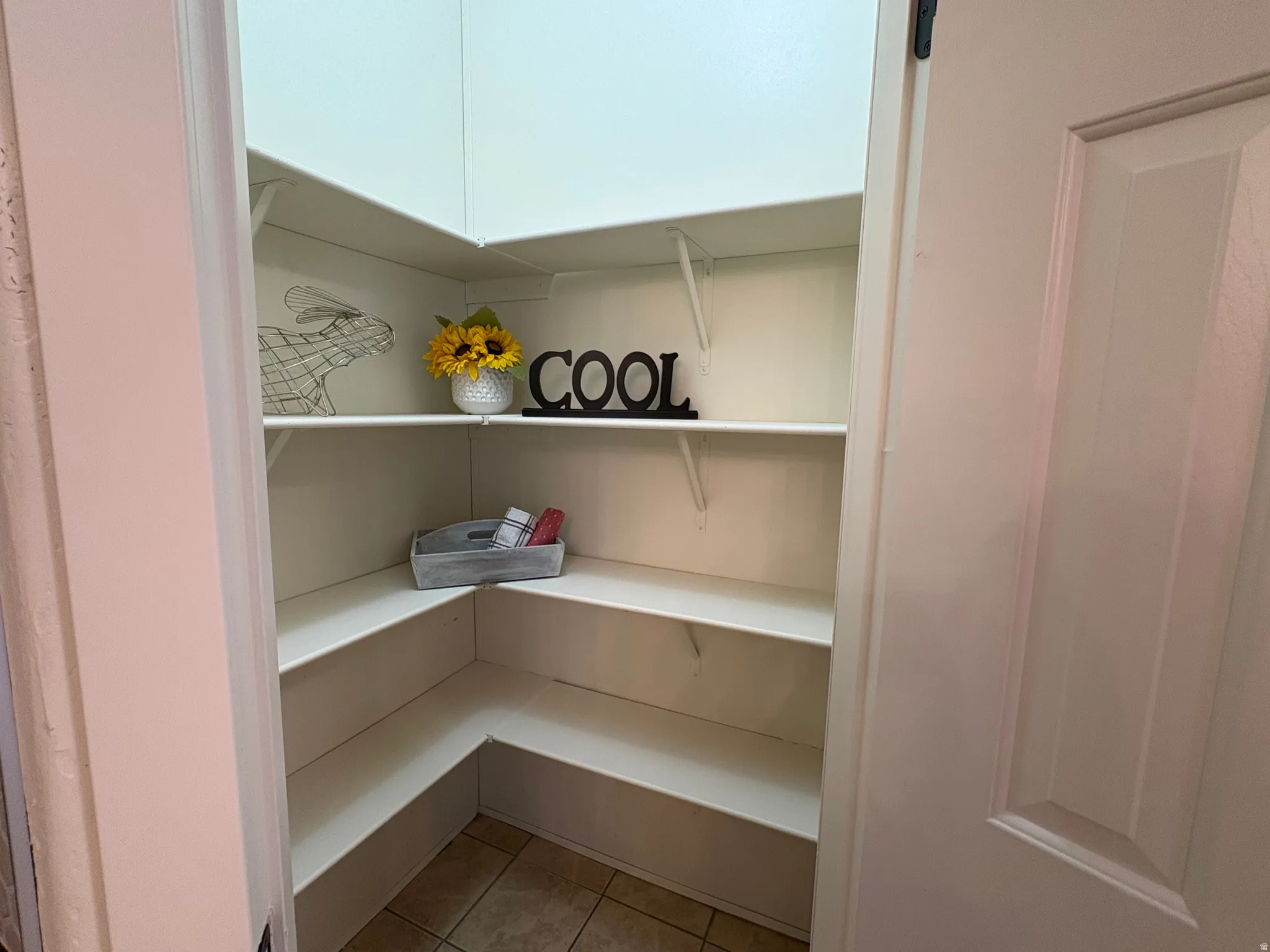 Corner pantry with white shelving and tile flooring