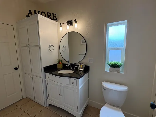 Bathroom featuring a white vanity with a black countertop, a circular mirror, and a three-light fixture