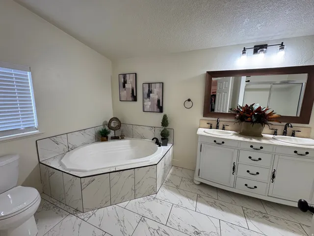 Bathroom featuring a corner soaking tub with marble-look tile surround and a double vanity with an integrated countertop and two undermount sinks
