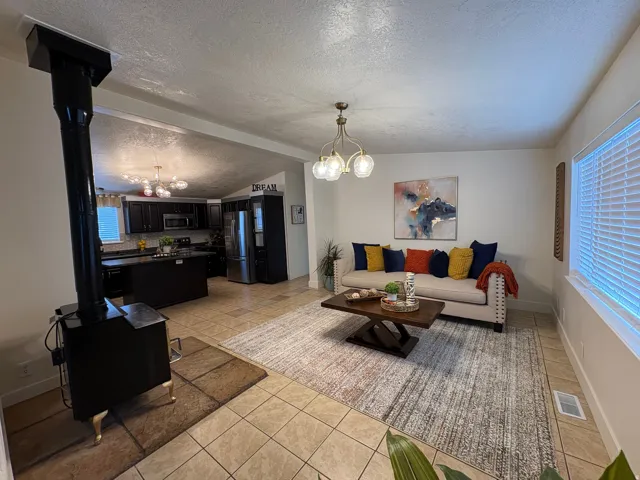 Open-concept living space featuring a black wood-burning stove, tile flooring, and a kitchen with dark cabinetry and stainless steel appliances