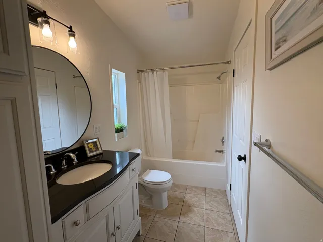 Bathroom featuring a white vanity with a dark countertop, an undermount sink, and a circular mirror