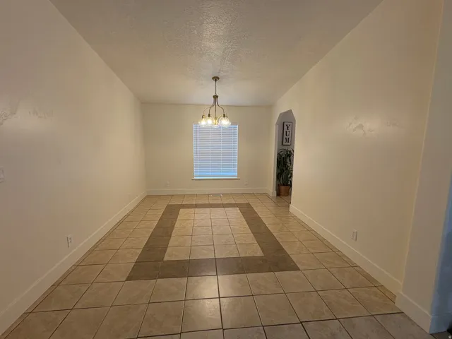 Spacious room featuring neutral-toned tile flooring with a darker accent border, a window with blinds, and an arched doorway