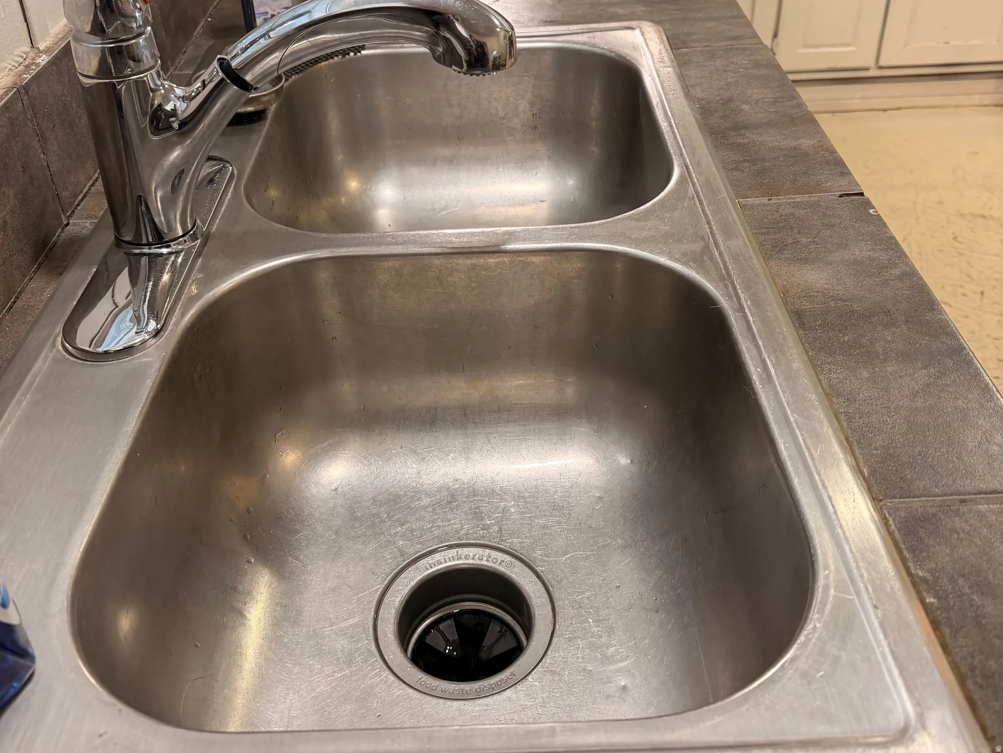 Stainless steel double basin sink with a chrome pull-down faucet, set into a tiled countertop